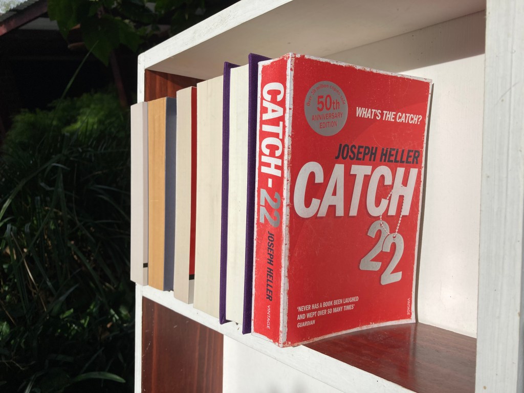 The novel Catch-22 on a bookshelf with several other books.