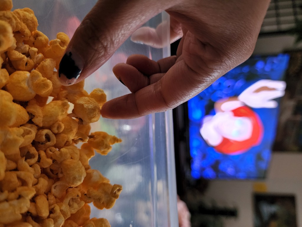 Hand grabbing popcorn with The Little Mermaid on display on the TV in the background.