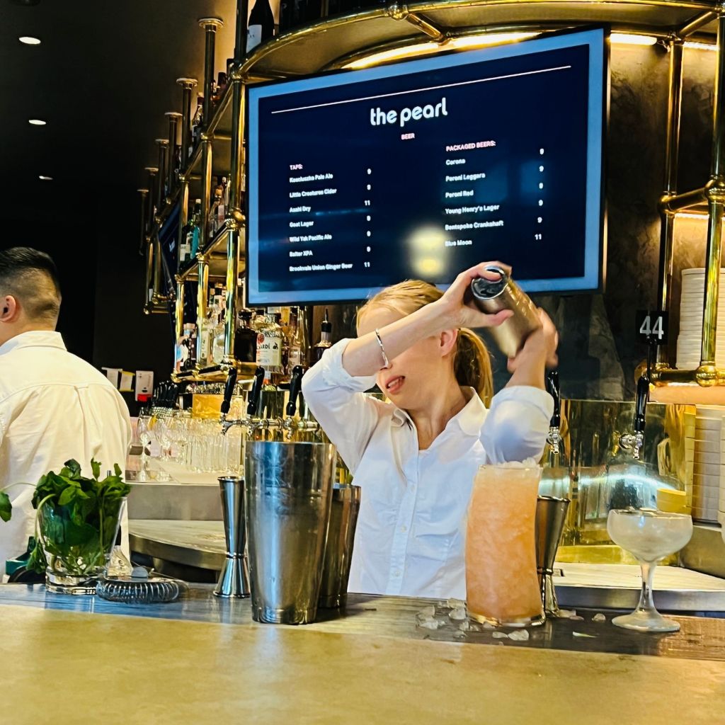 Bar staff shaking a cocktail over her shoulder getting ready to pour it into a glass