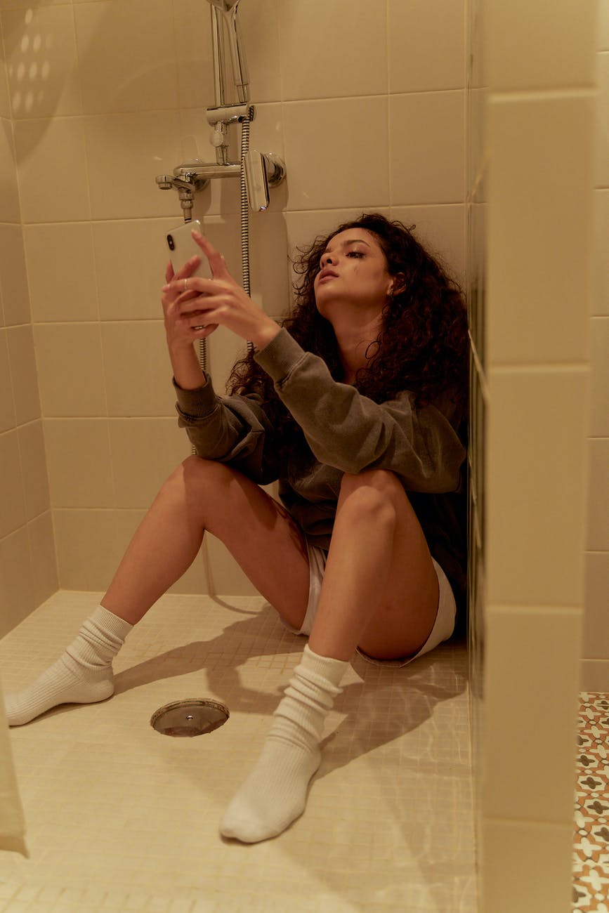 a woman sitting alone on the bathroom floor while using her smartphone