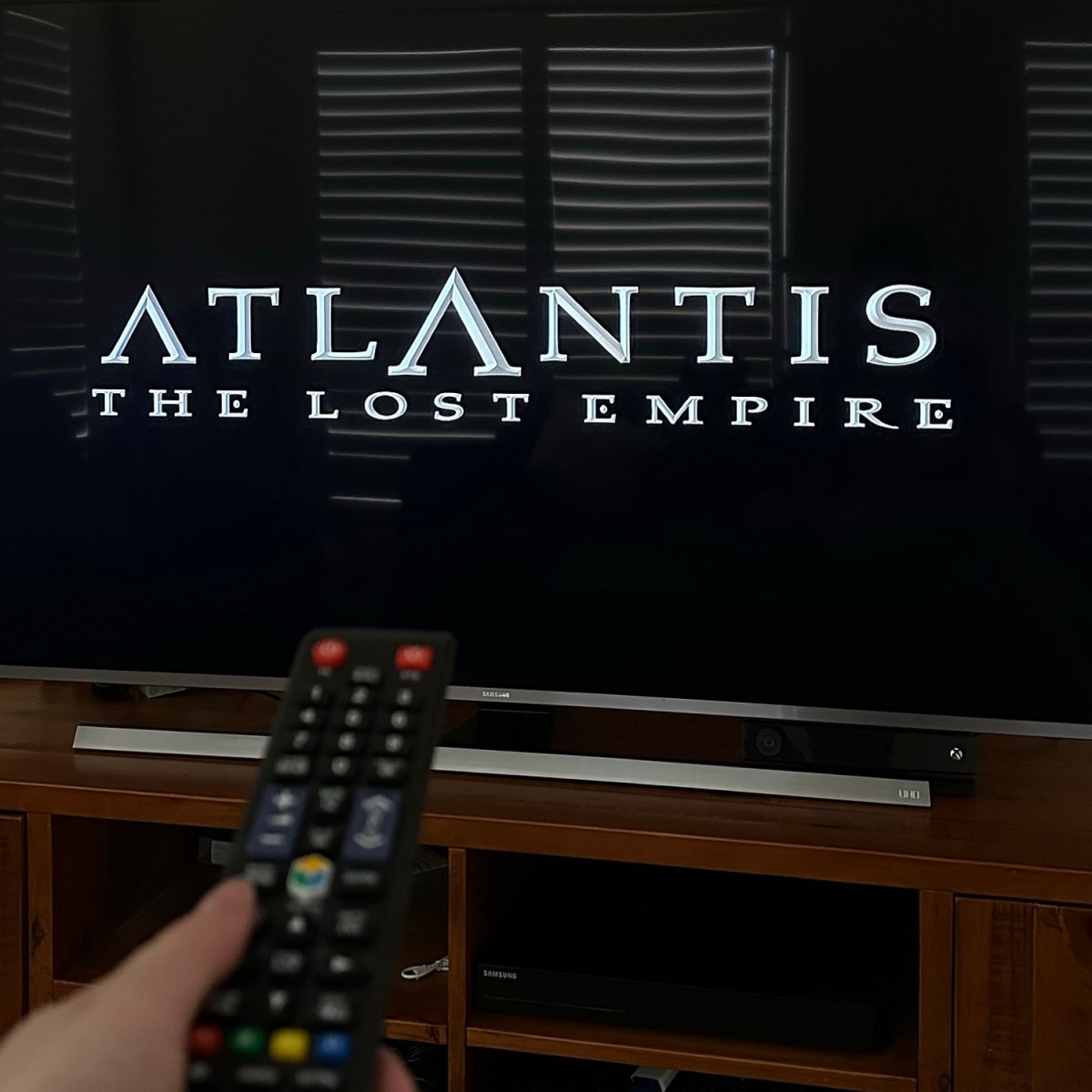 Title screen on TV saying Atlantis The Lost Empire. TV remote is pointed at the screen.