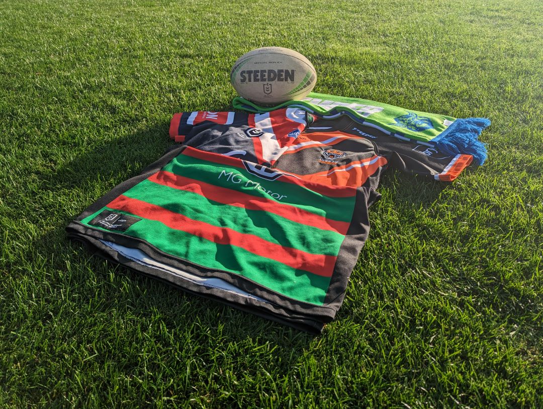 NRL ball on ground with Sydney Rooster, South Sydney Rabbitohs and a Wests Tigers Jersey
