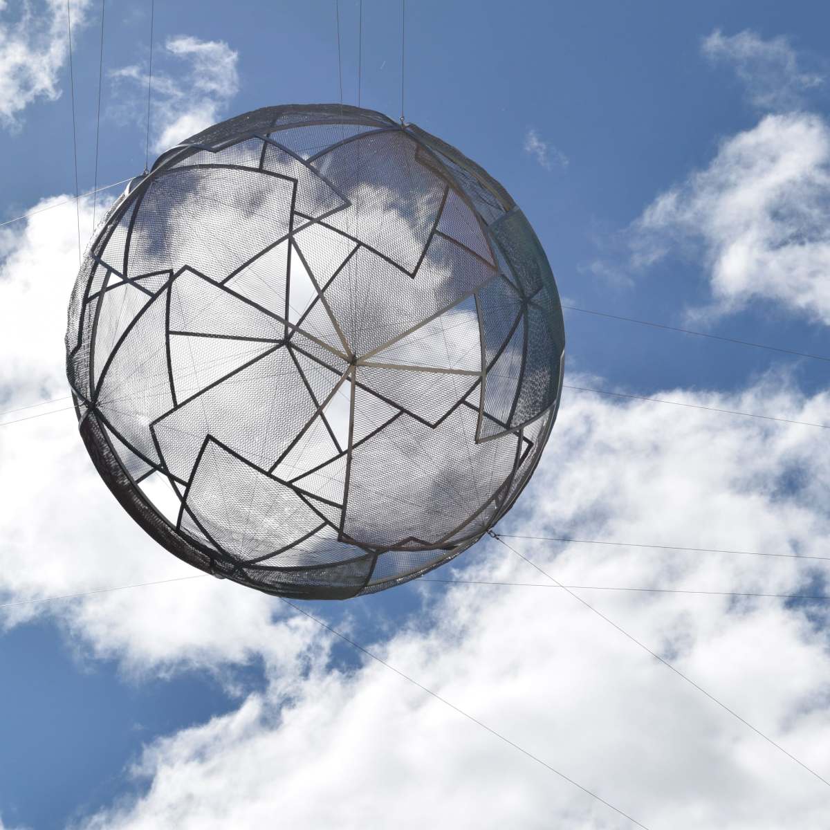 A metal sphere suspended in the air against a blue sky with clouds