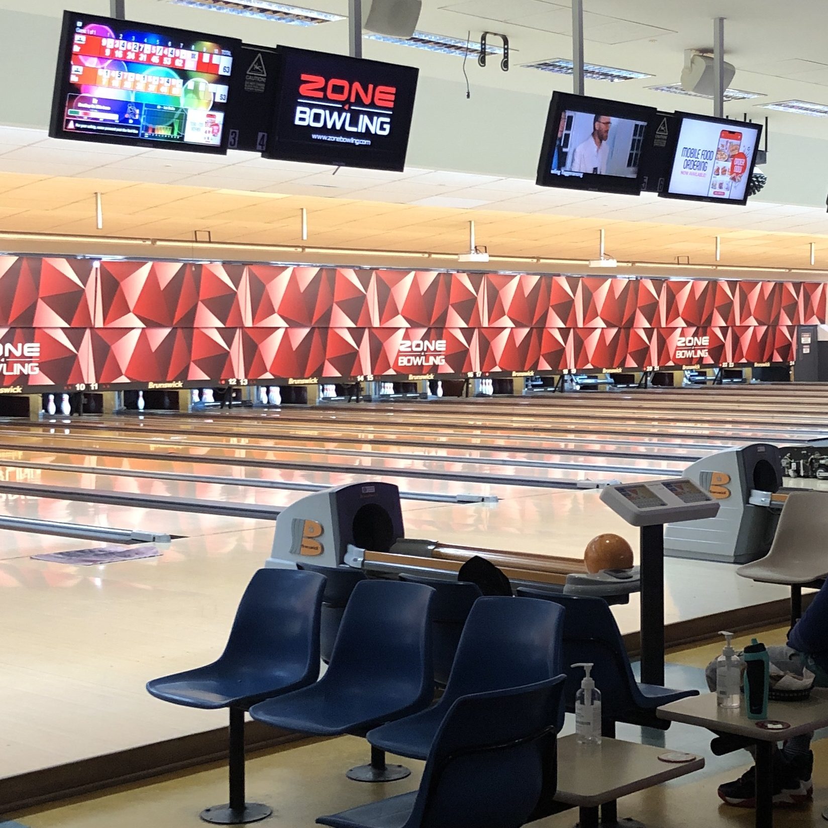 photo of a bowling alley with lanes, a call, some seats and tvs with scores on them