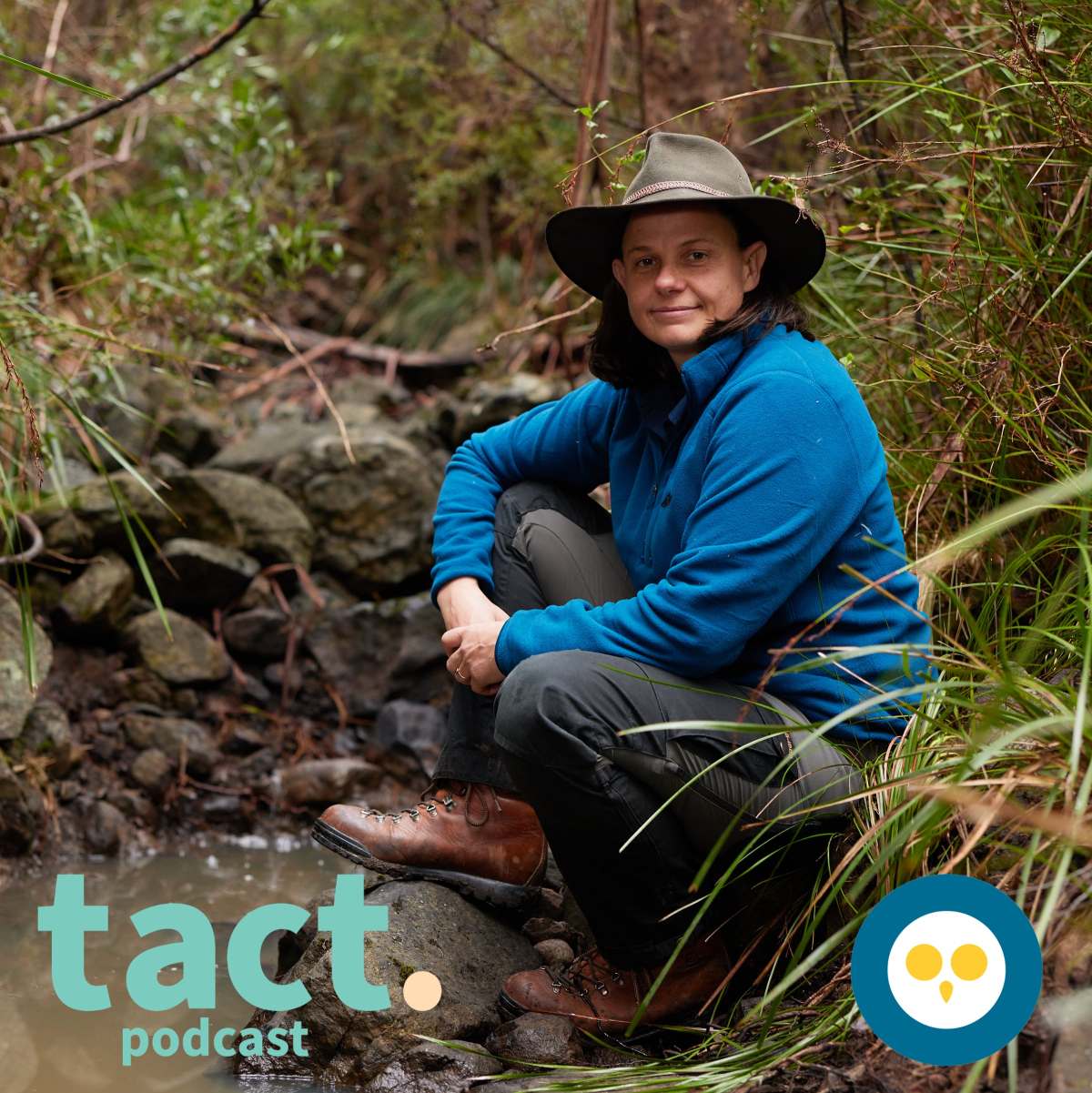 Alone Australia's Kate Grarock sitting beside a stream in the bush smiling at the camera, with The Owl and TACT logos
