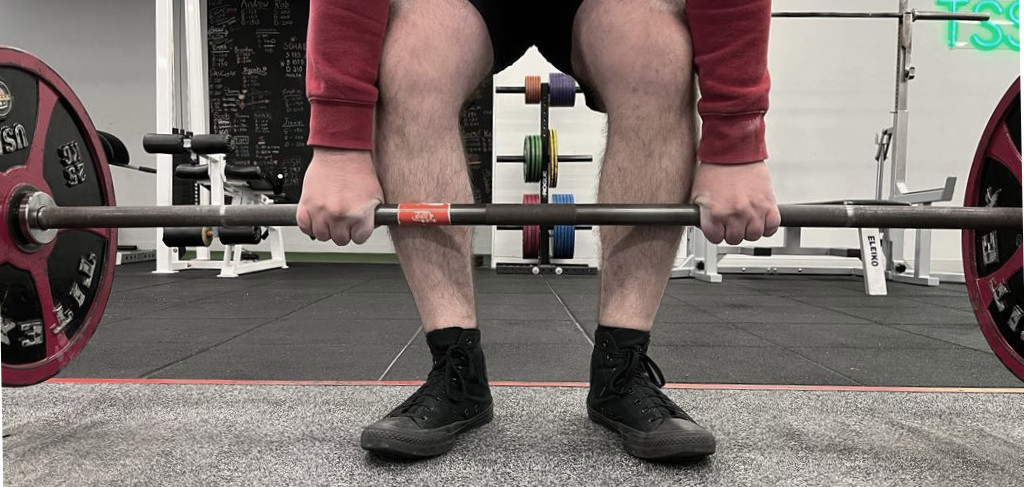 A landscape picture of MacAlonan's legs and hands lifting some weights in a squat. 