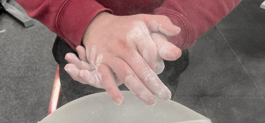A landscape picture of MacAlonan's hands as he applies chalk, with clouds of chalk dust. 