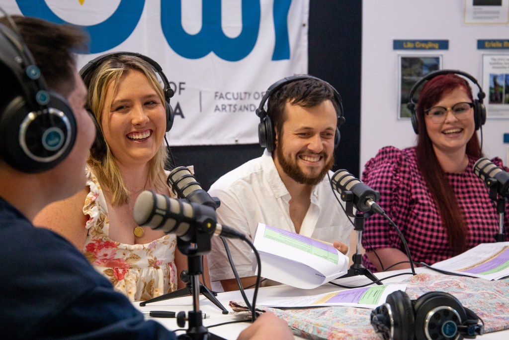Hosts Maddi, Ben and Lila smiling behind their microphones