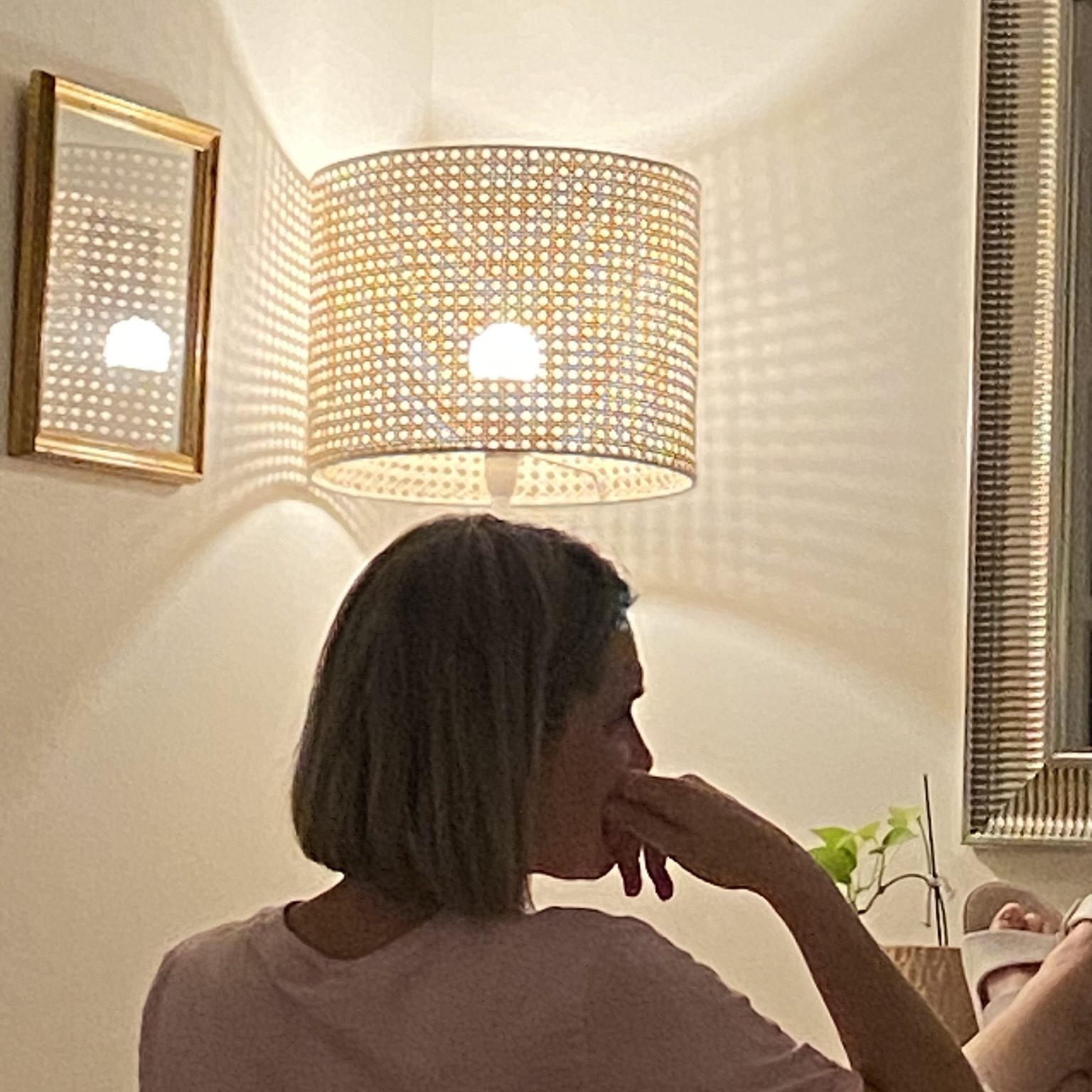 A photo of Mel Kent posing contemplatively away from the camera. A lamp above her head illuminates a halo-like light around her.