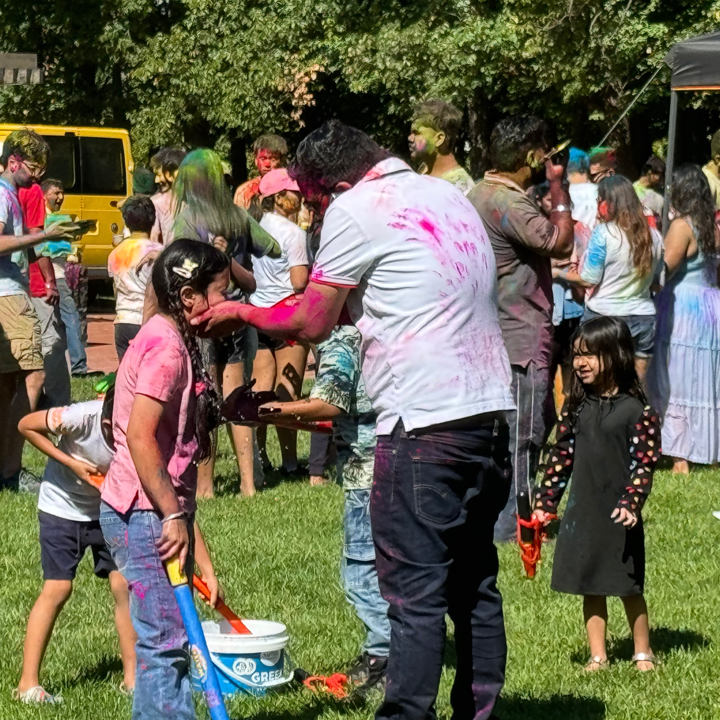 man wipes girl's face with water and kids fill up water guns in the background