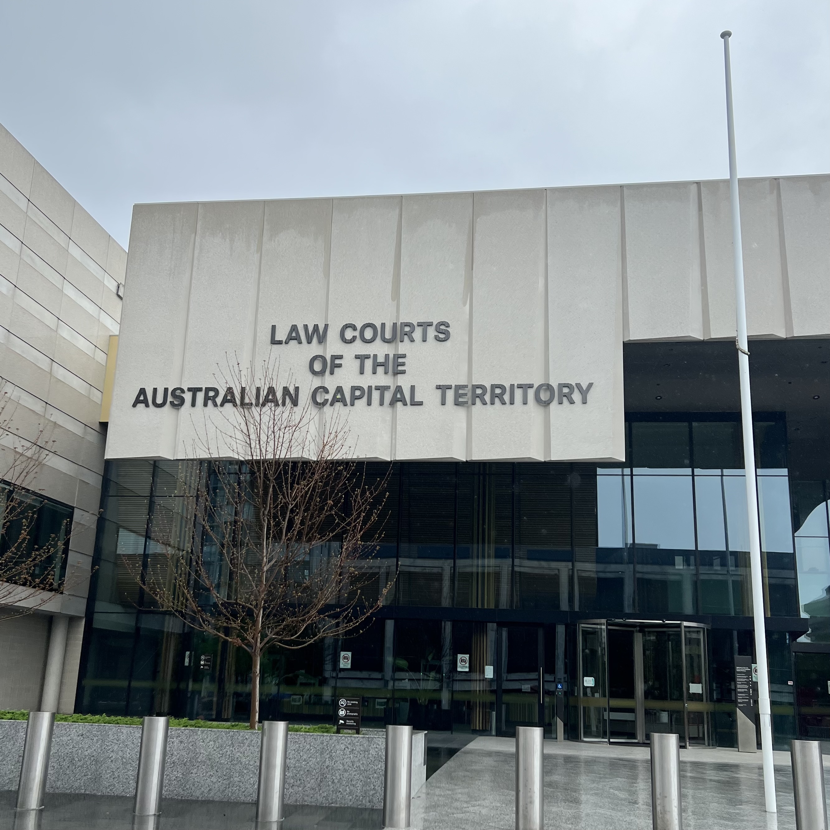 Picture of the front of the Law Courts of the Australian Capital Territory taken in the rain. Tree with no leaves in front.