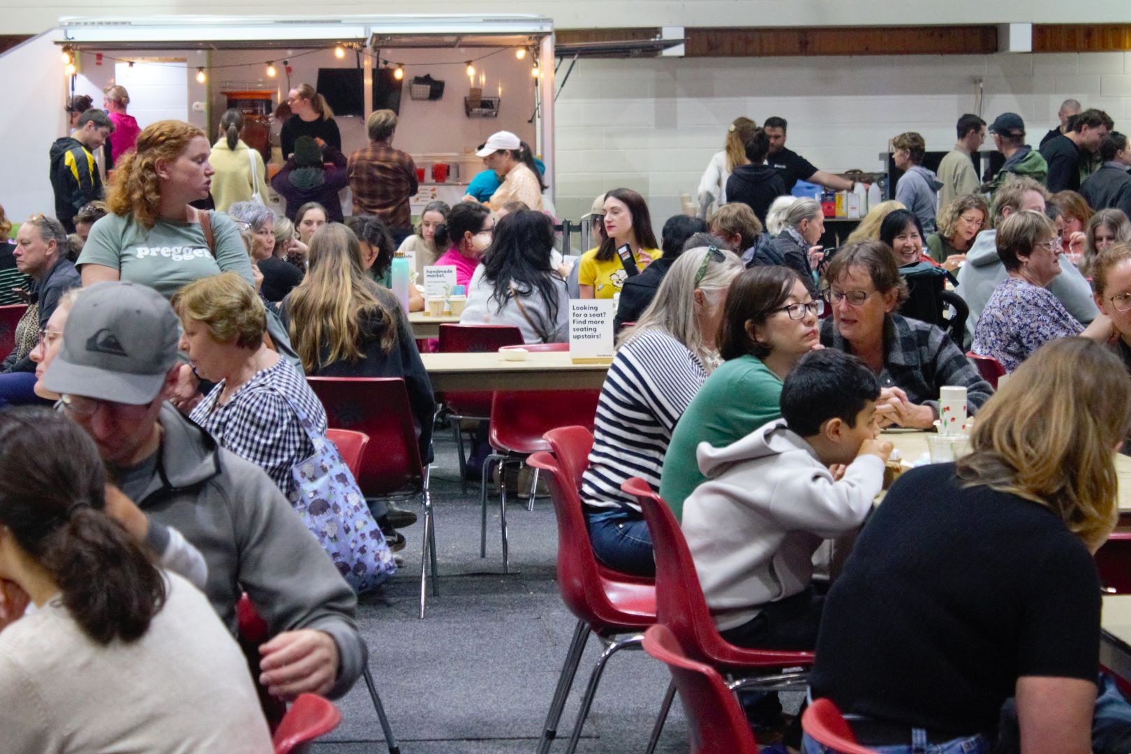 A crowd of people sitting in red chairs at a market food court