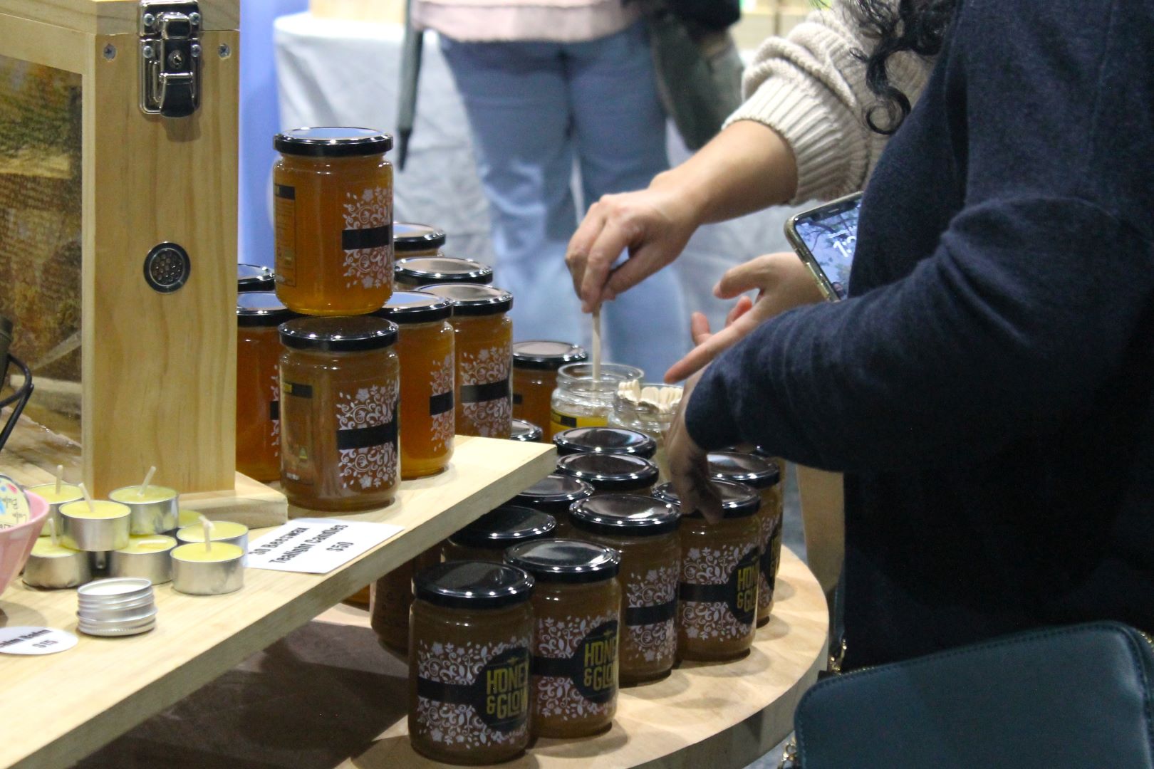 A woman dipping a stick into a tester jar of honey. 