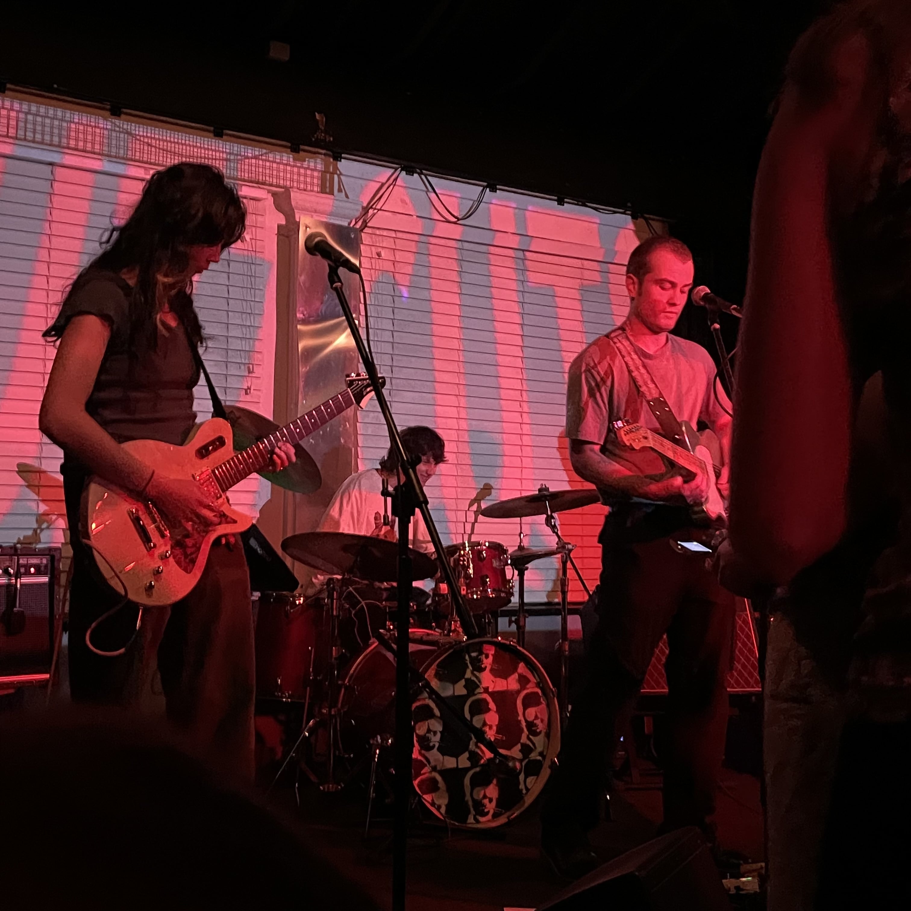 Band on stage. One guitarist is on the left, the other on the right. The drummer peers through the middle.