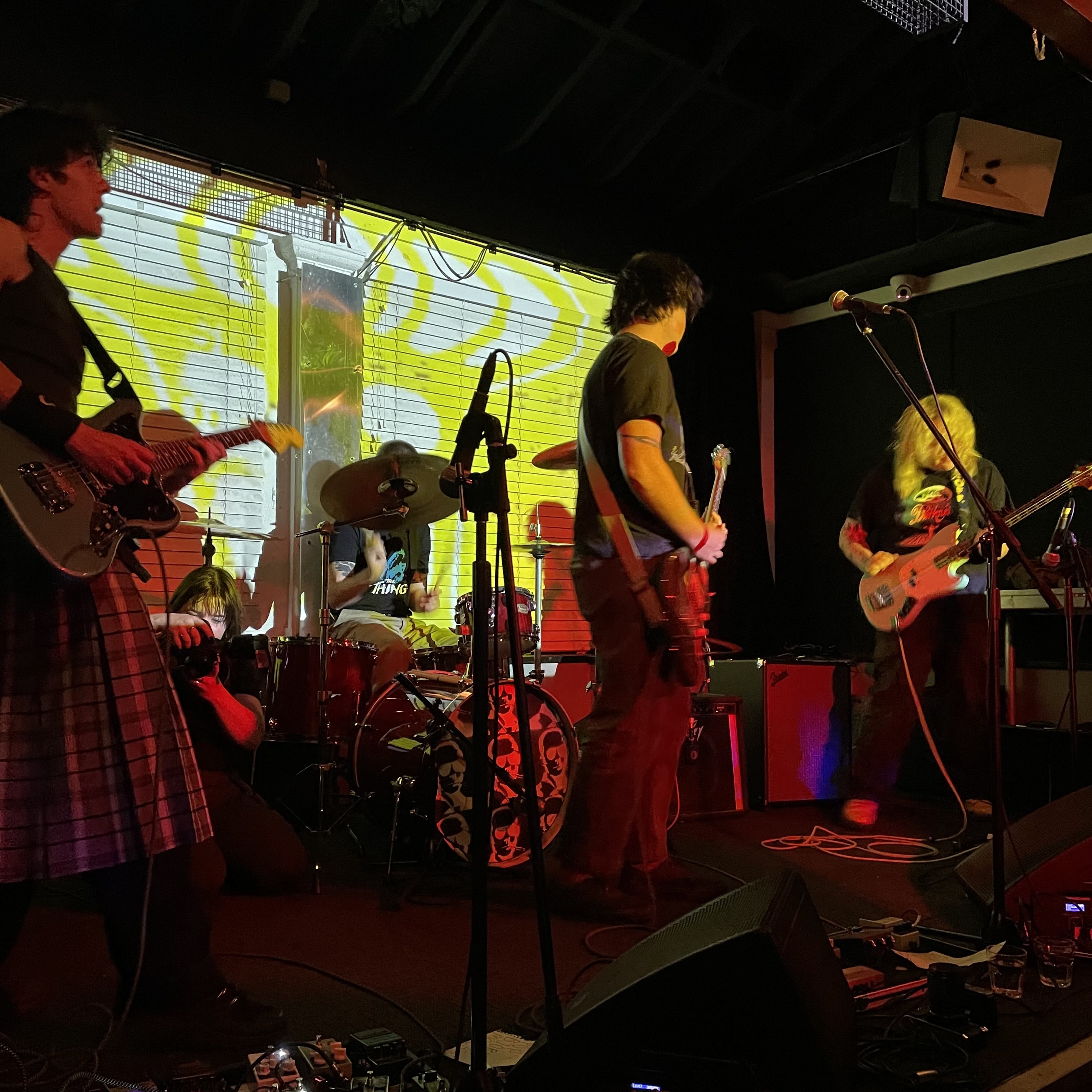Band on stage with yellow lighting on them. A guitarist in a kilt is to the left, another in the middle and other on the right.