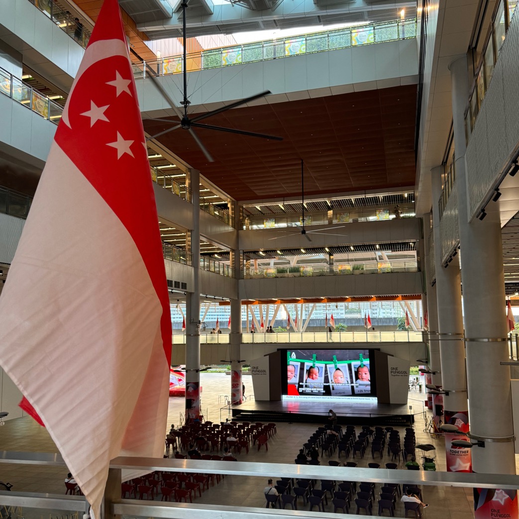 a Singapore flag attached to a ledge with a screen and chairs in the background 