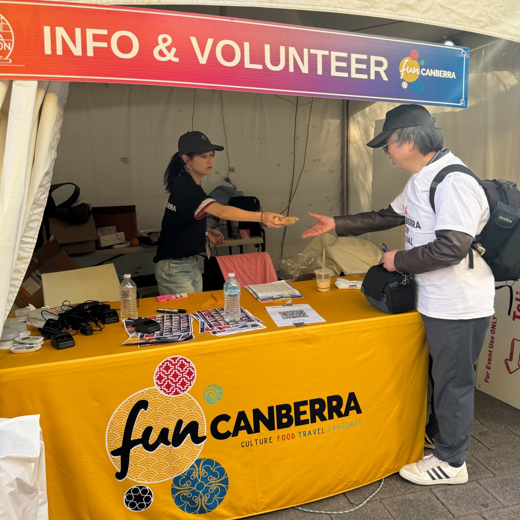 Info and Volunteer stall of fun Canberra with woman giving a moon cake to a man 