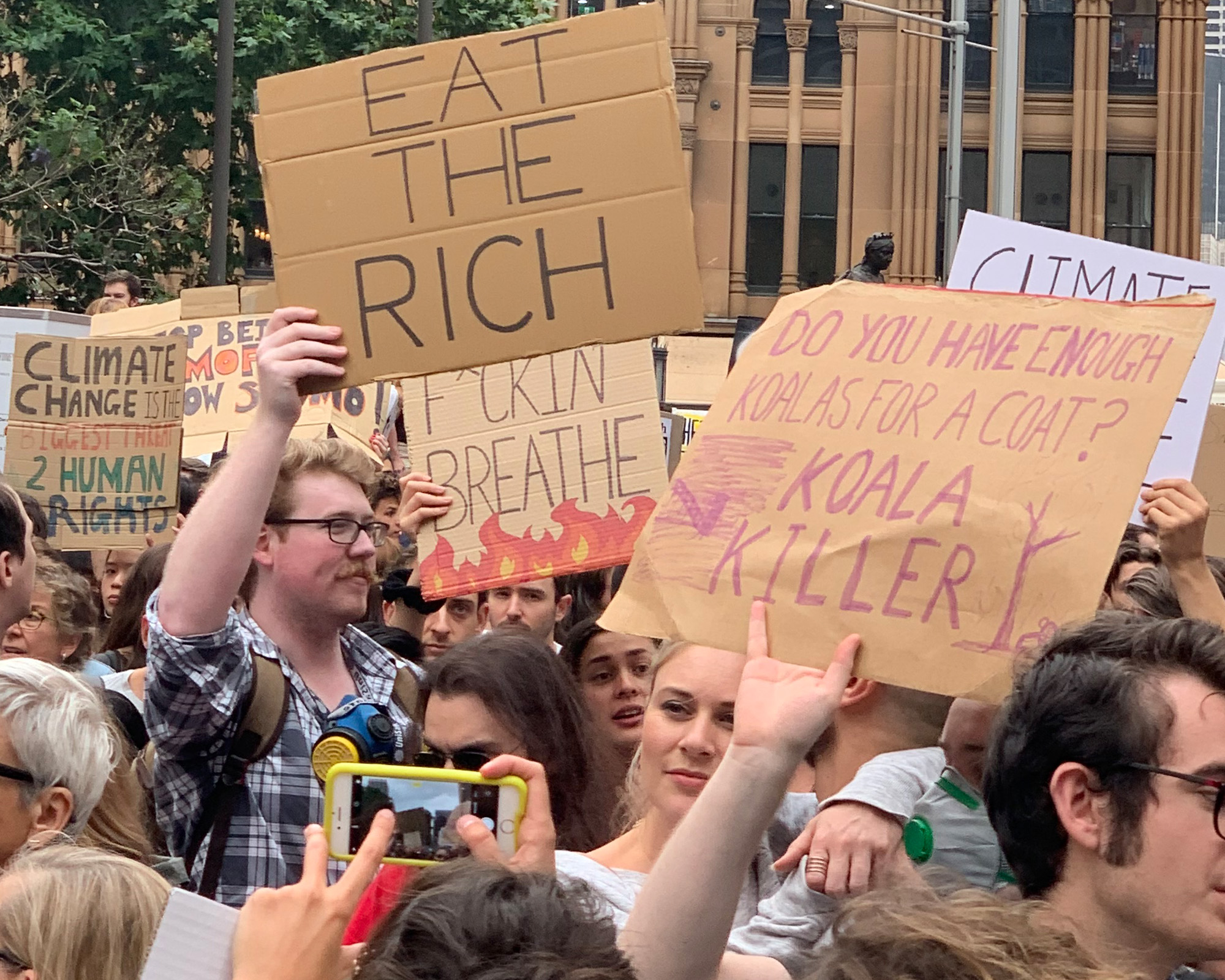 A crowd of protestors holding signs saying "Eat the rich", "Koala killer" and "climate change is the biggest threat 2 human rights"