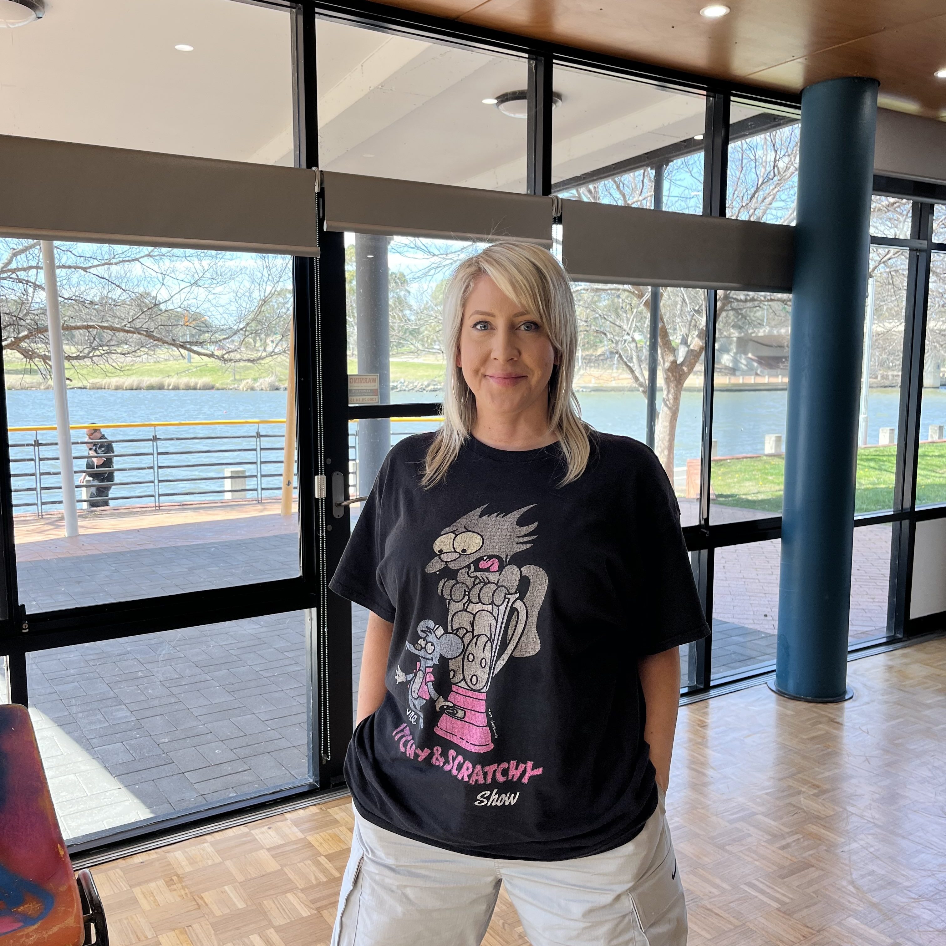 Women with straight blonde hair wearing a black t-shirt stands in an empty dance studio
