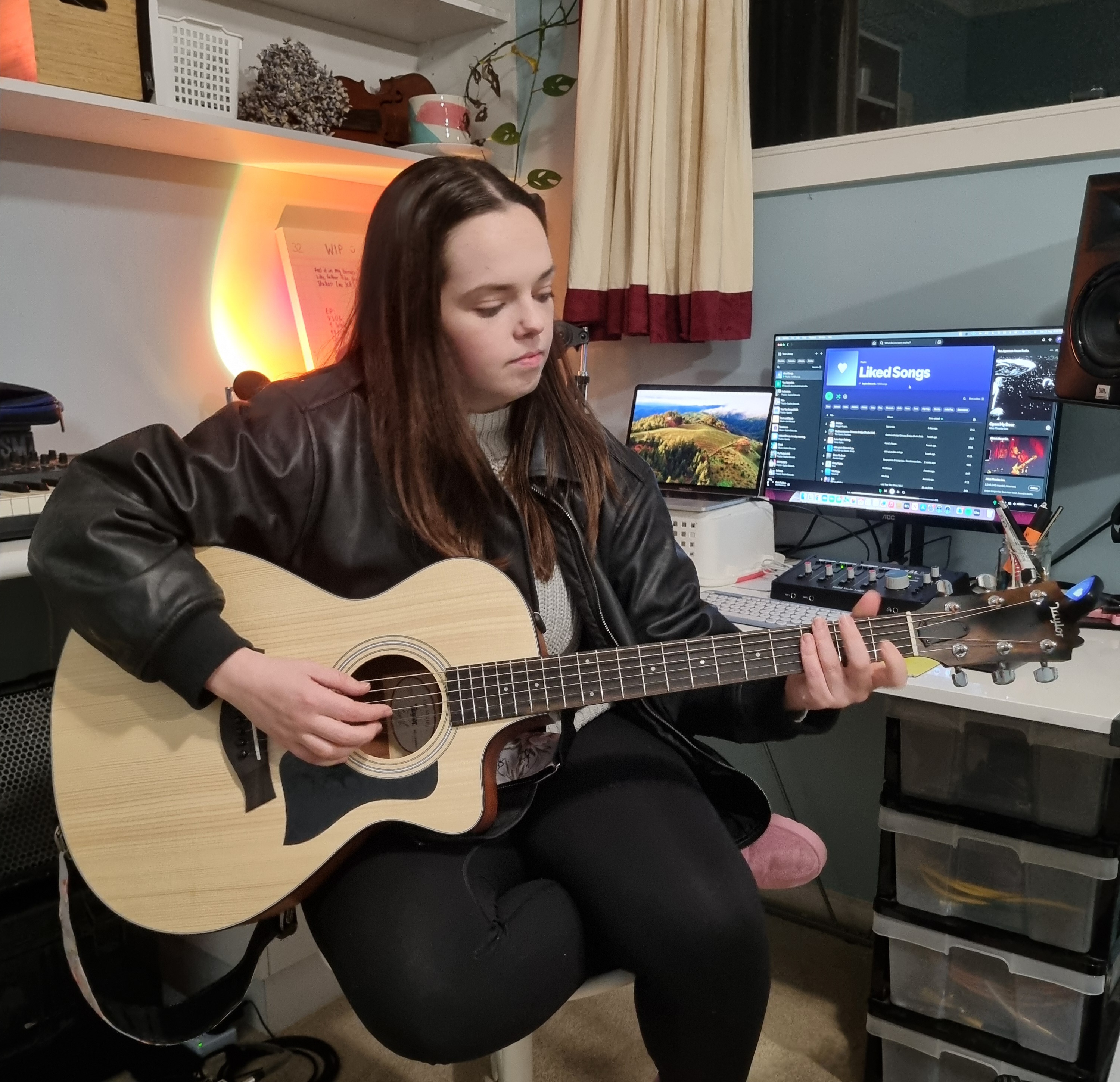 Sophie, seated at her desk inside her home studio, playing guitar