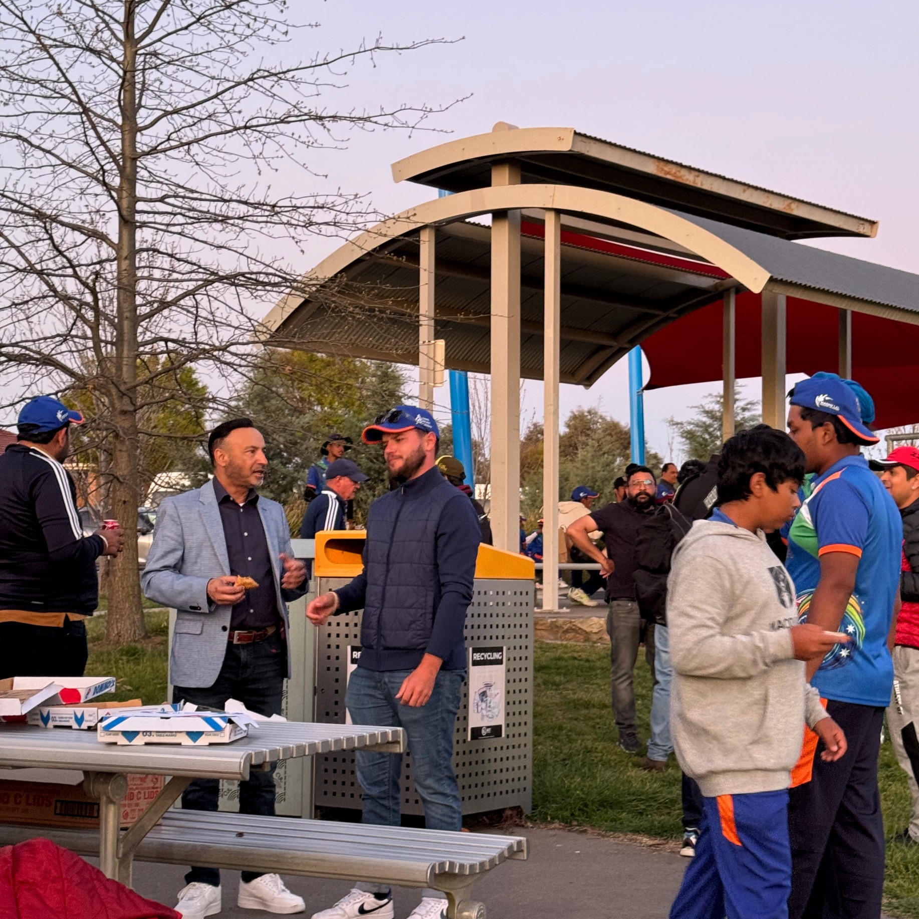 people standing around picnic table and holding pizza