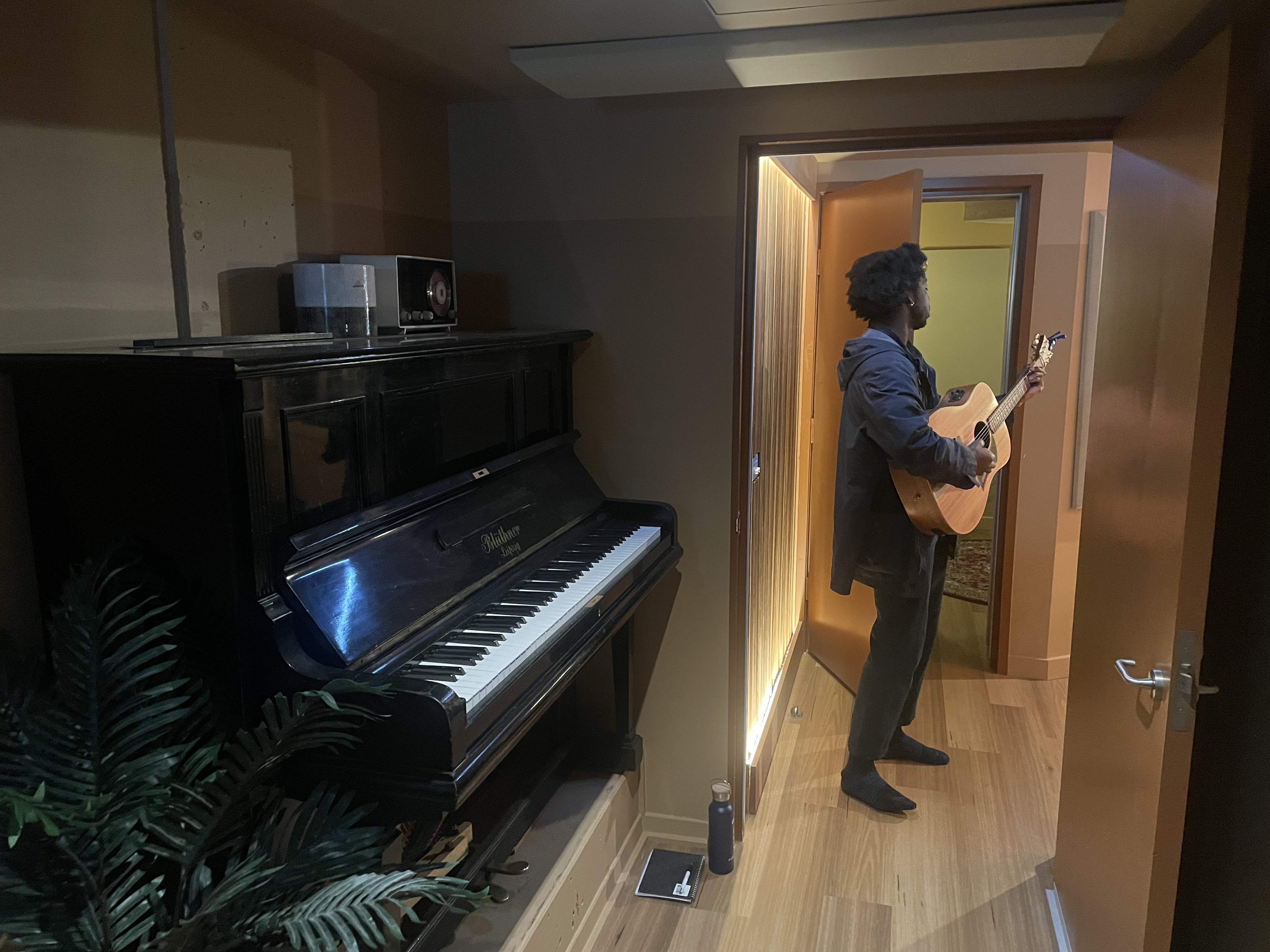 Man playing the guitar in a doorway with a piano behind him. 