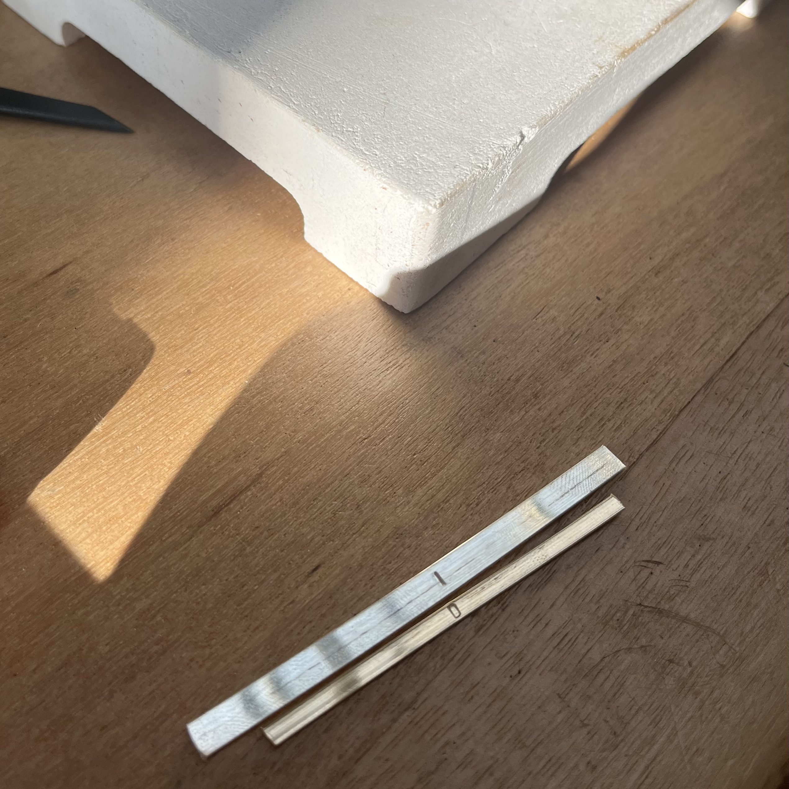 Two strips of silver and cold with pressed initials on wooden table.