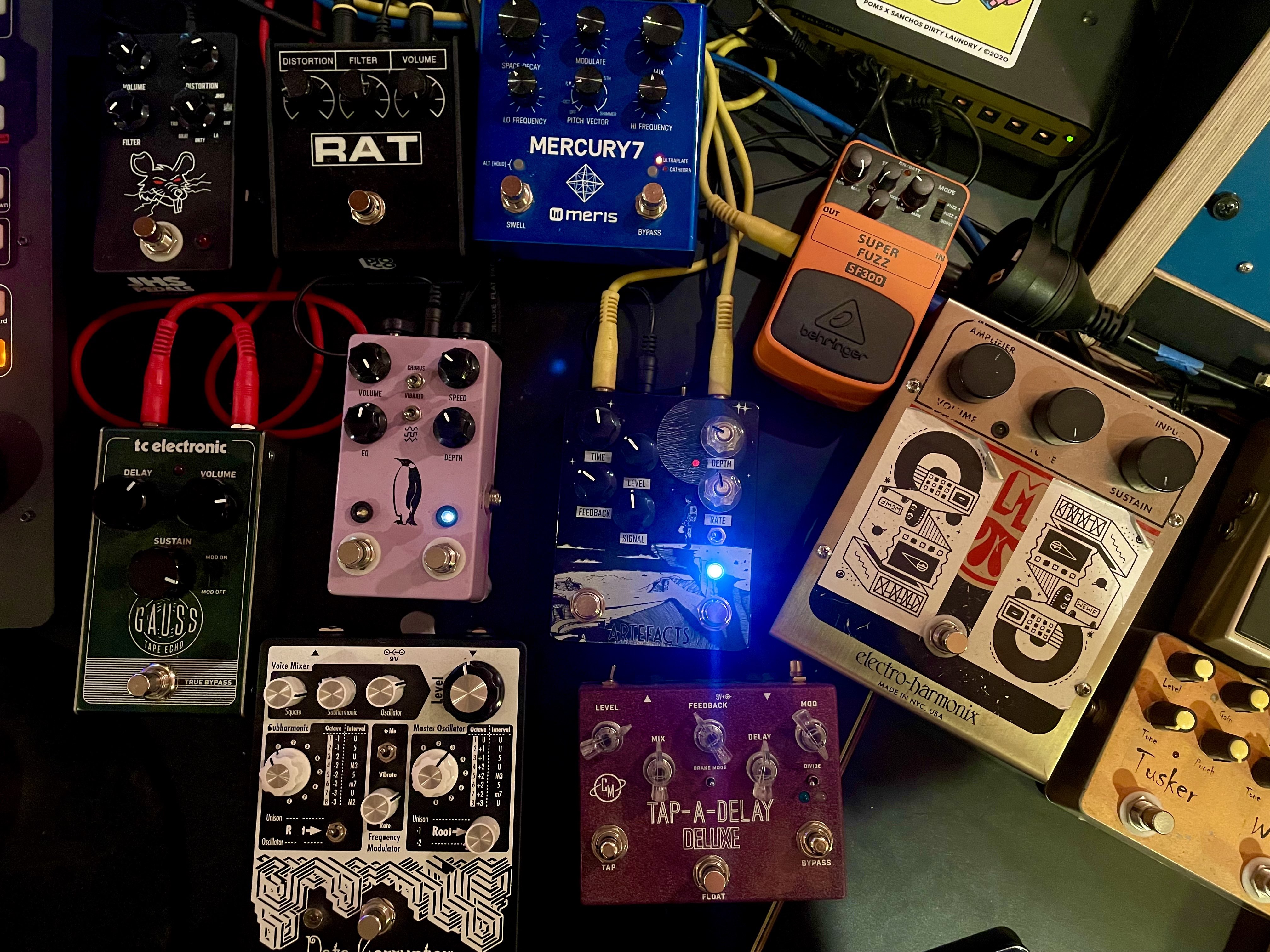 An arrangement of guitar pedals of various sizes and colour sitting on a desk.