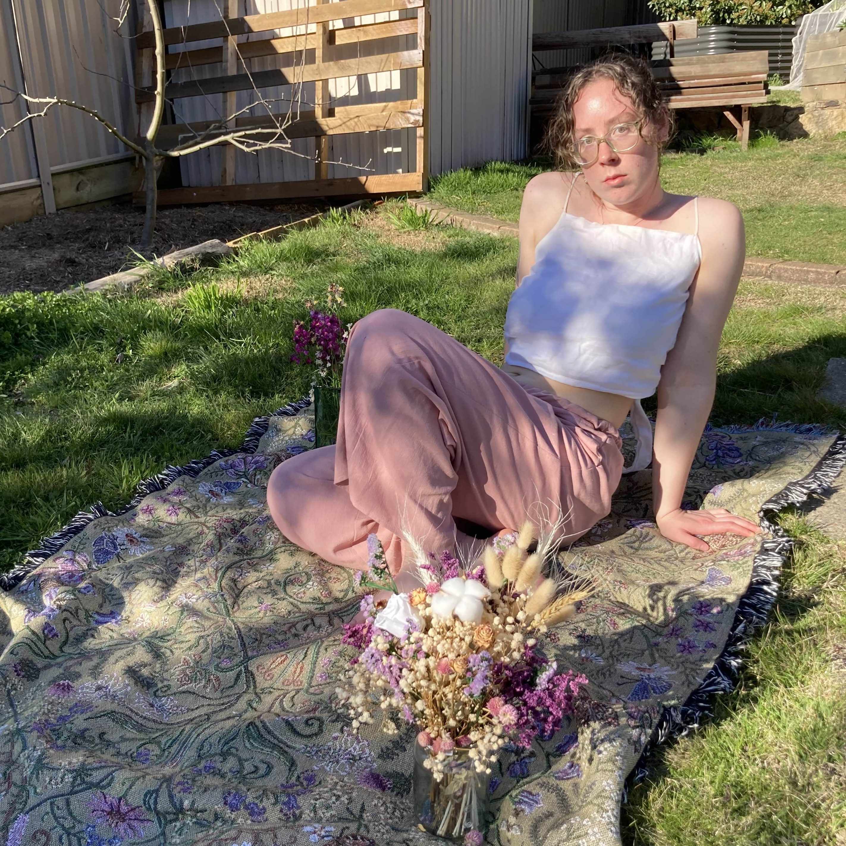 Sophie posed and sitting on a handmade blanket modeling a shirt and trousers from her brand