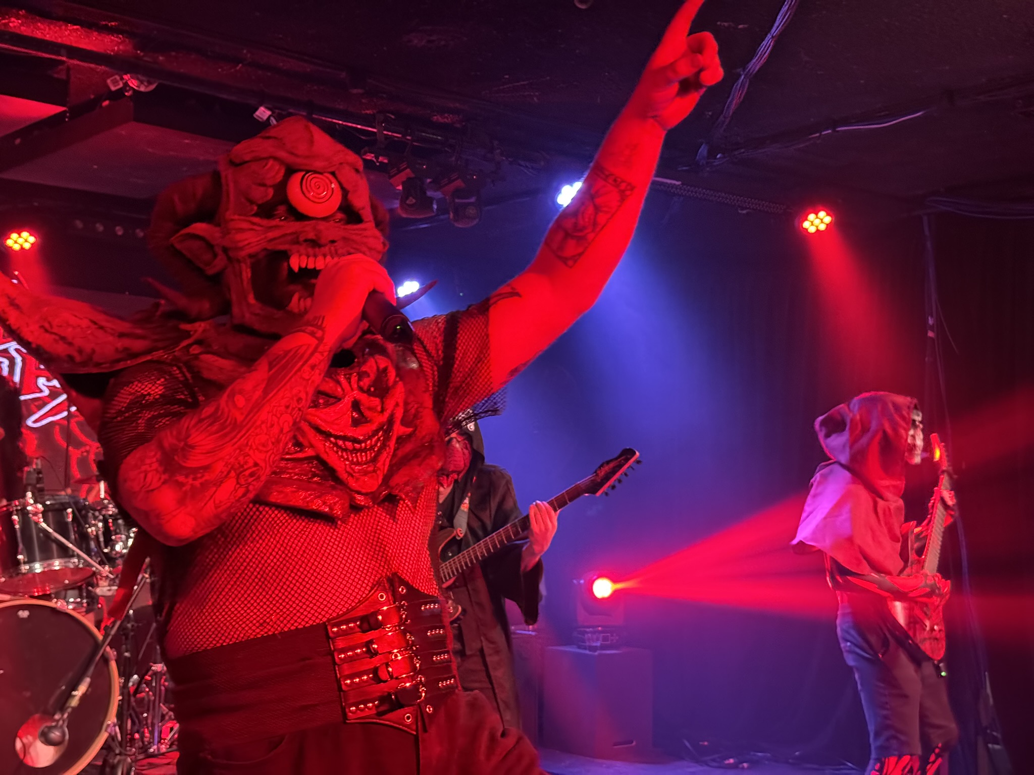 Shu Nagua during their opening song, with their lead singer in the foreground wearing a mask of a demon with one eye