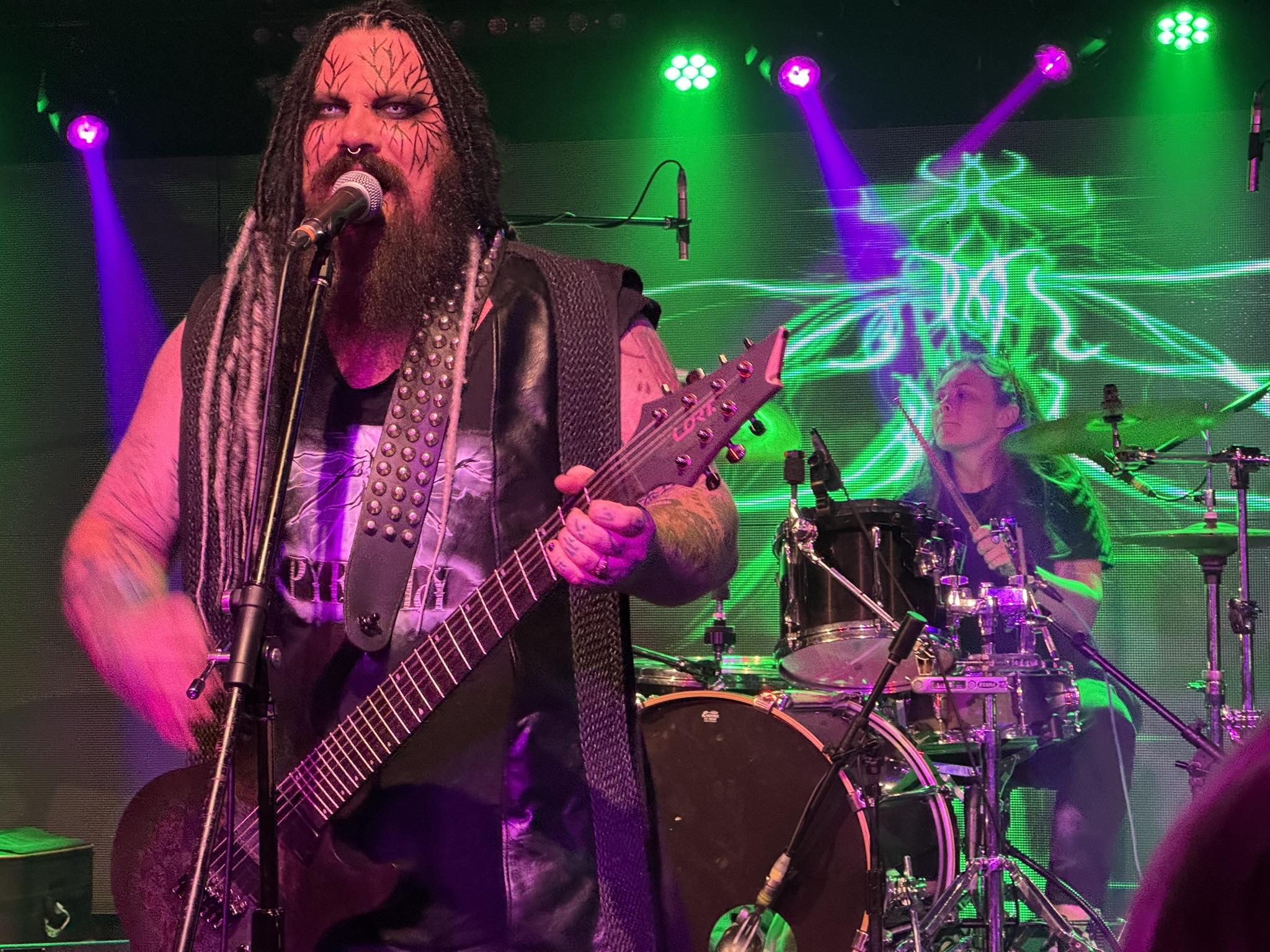 The lead singer and drummer of Pyrefly performing, with thelead singer wearing distinctive facial makeup like tree roots