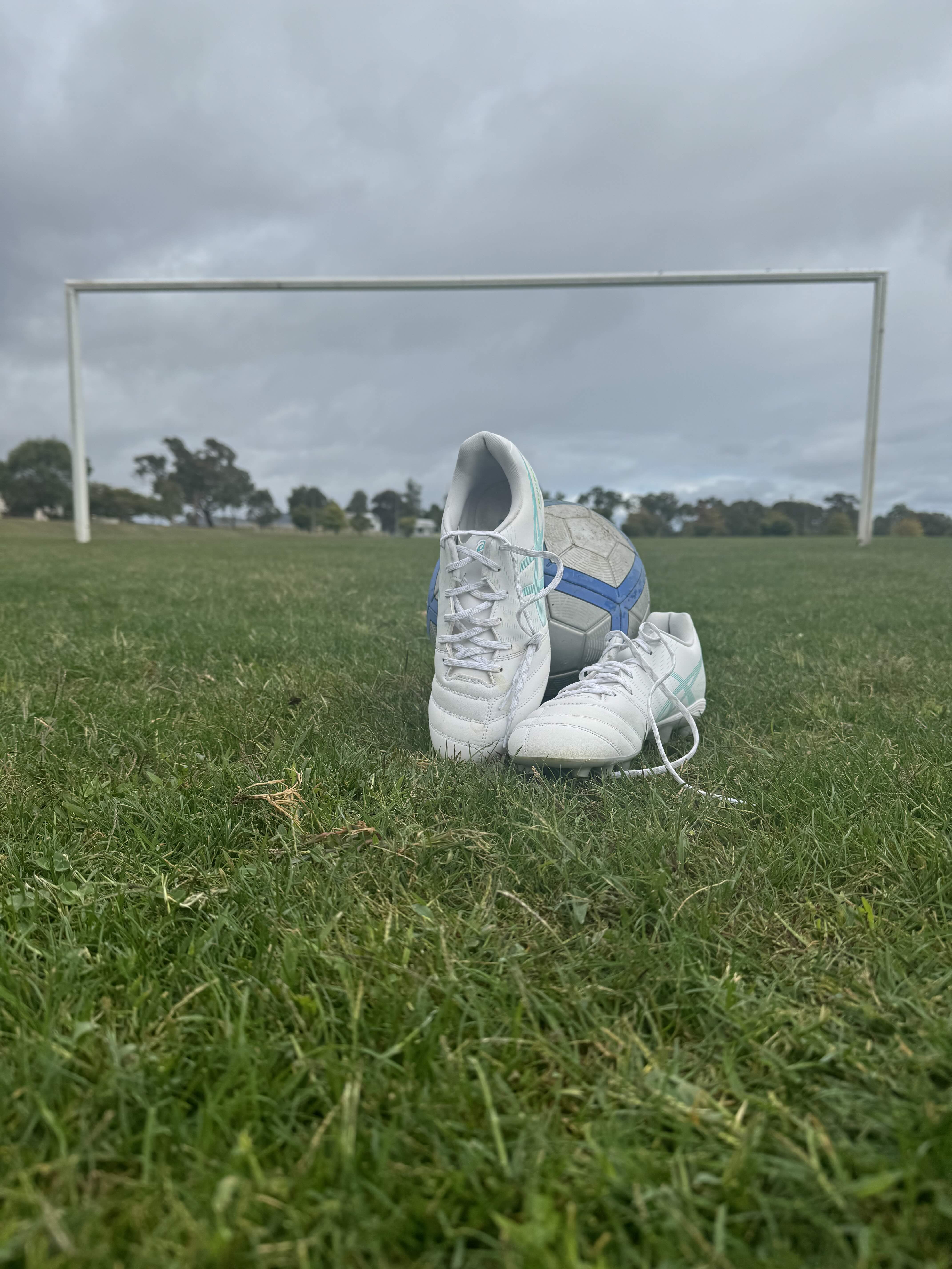 Soccer boots and ball with a soccer goal in the background. 