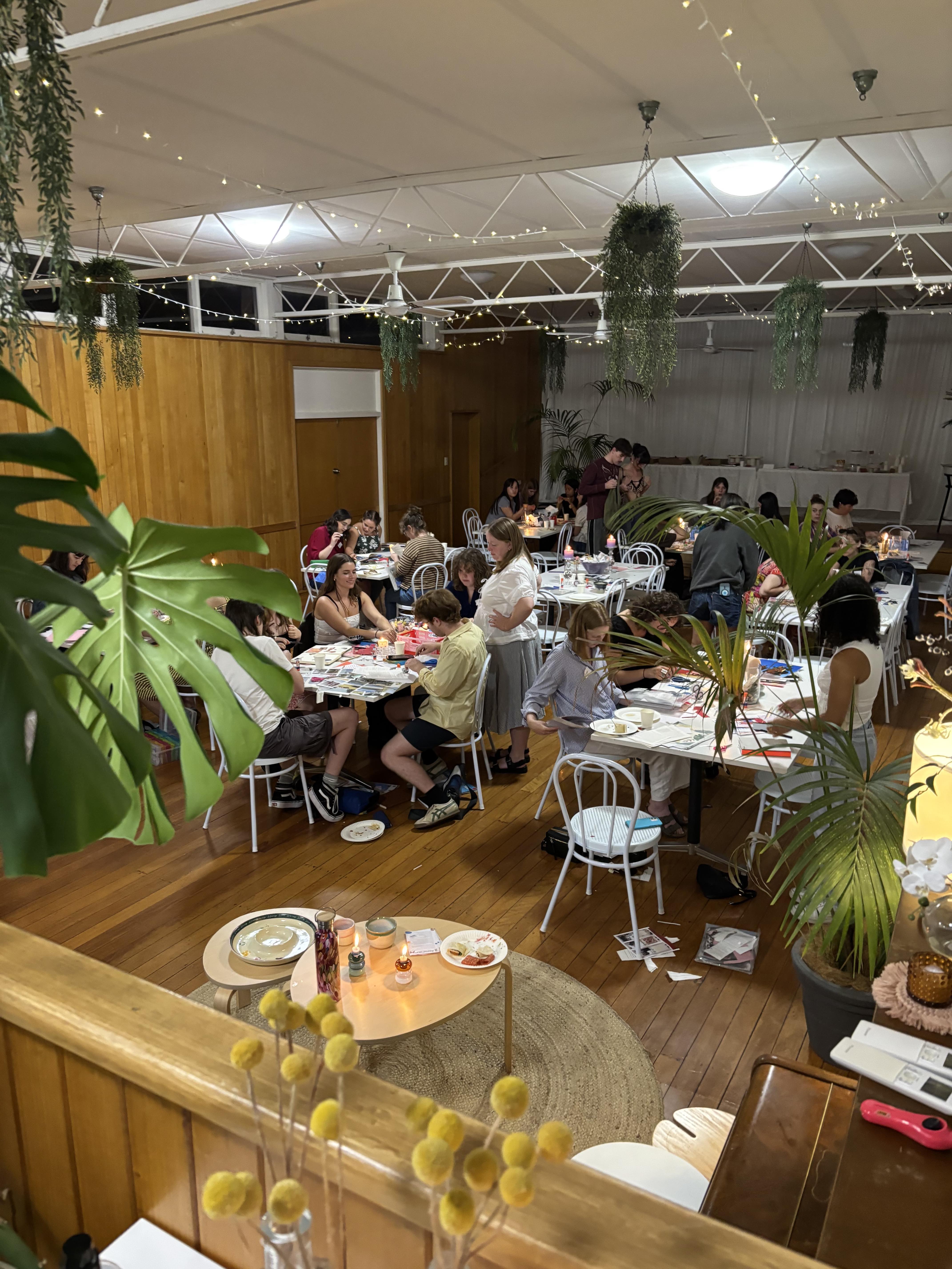 A hall with fairy lights on the roof and tables and chairs filled with people scrapbooking at Scrap Society.