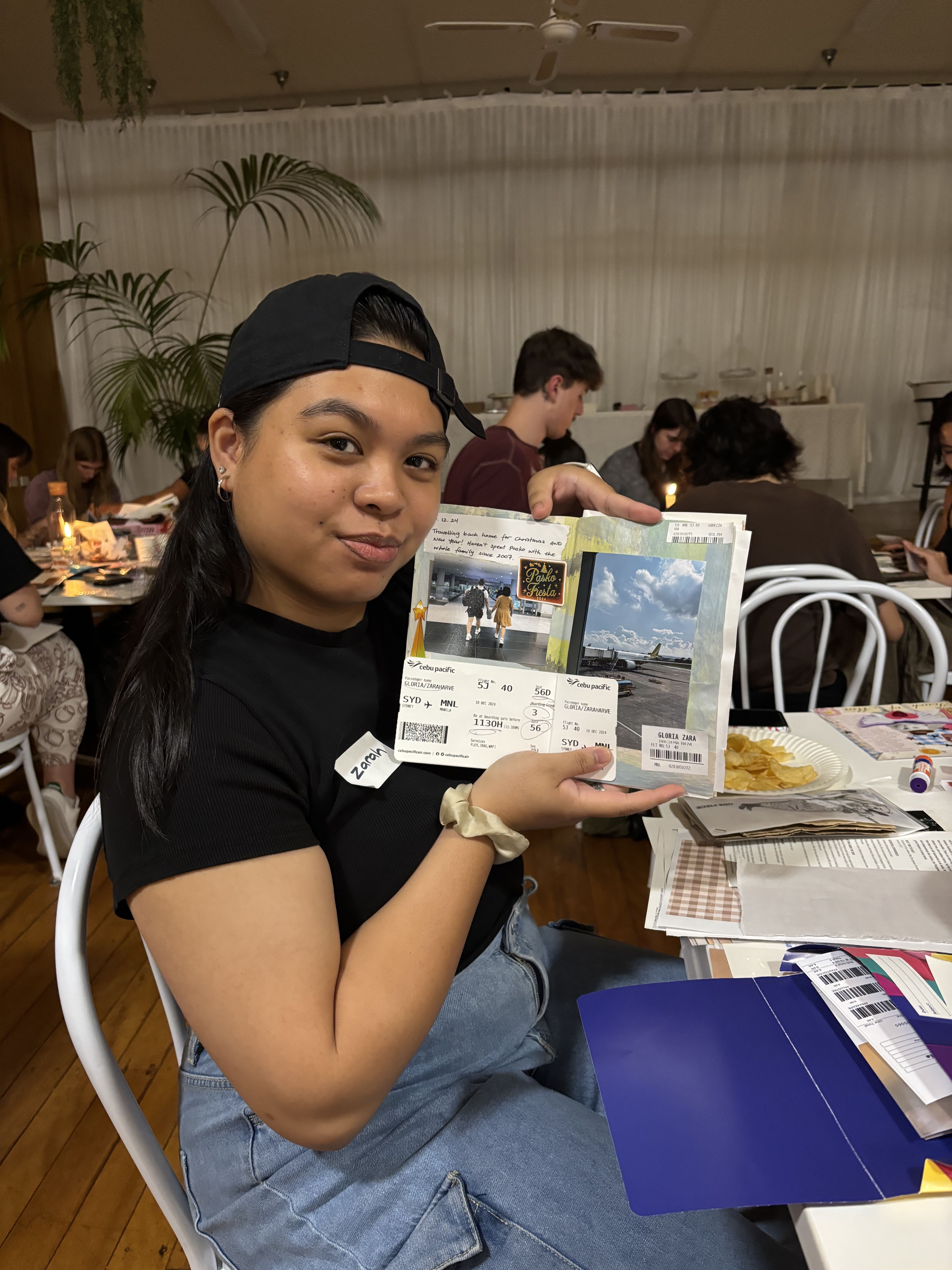 A woman in her 20s holds her journal up for the camera. The journal shows a plane ticket and photos from a recent trip