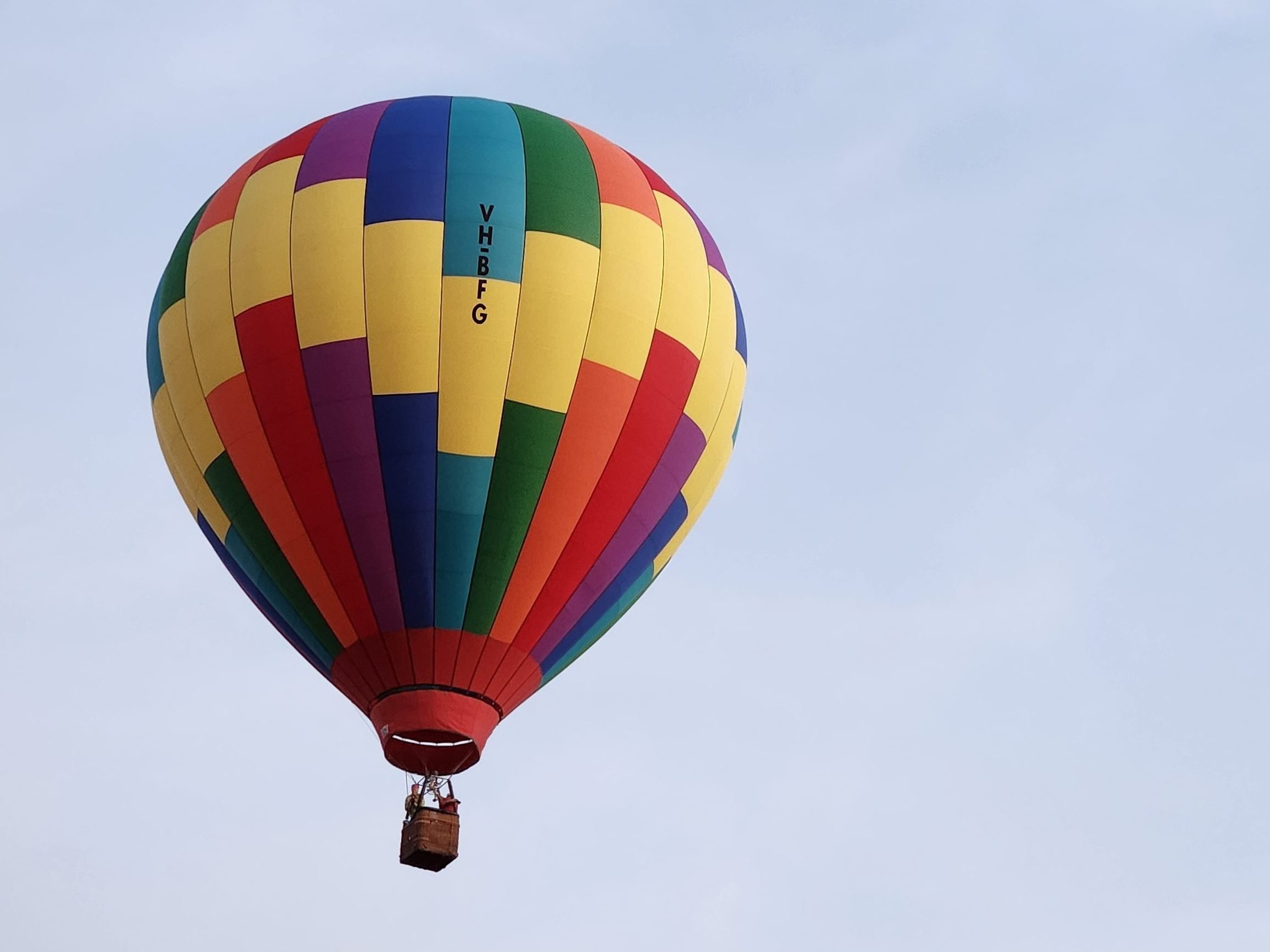 A vibrant hot air balloon with colourful panels soaring against a clear sky, showcasing its patterned design and basket below.