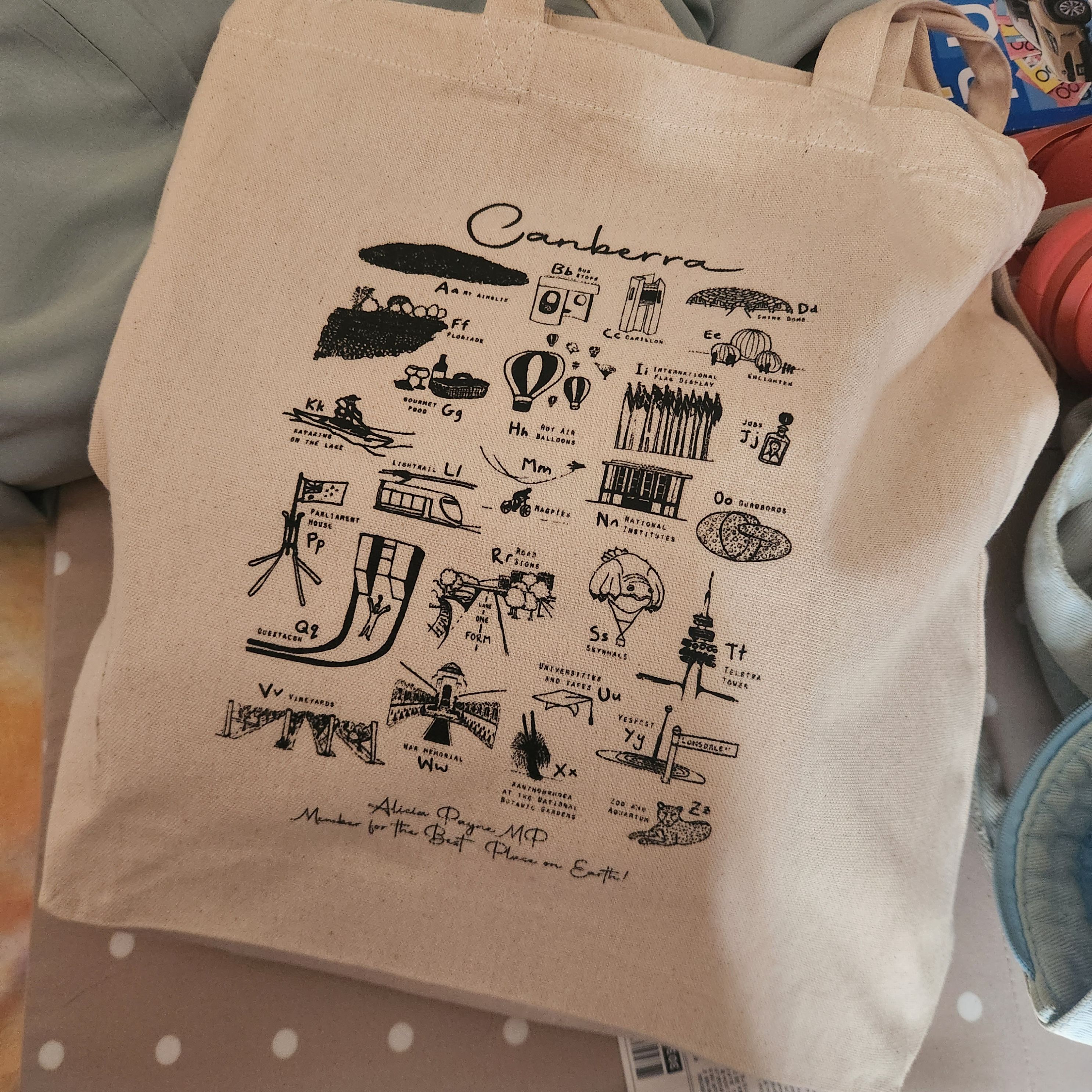 A tote bag with an A-Z of Canberra landmarks made in partnership with refugee women living in canberra.