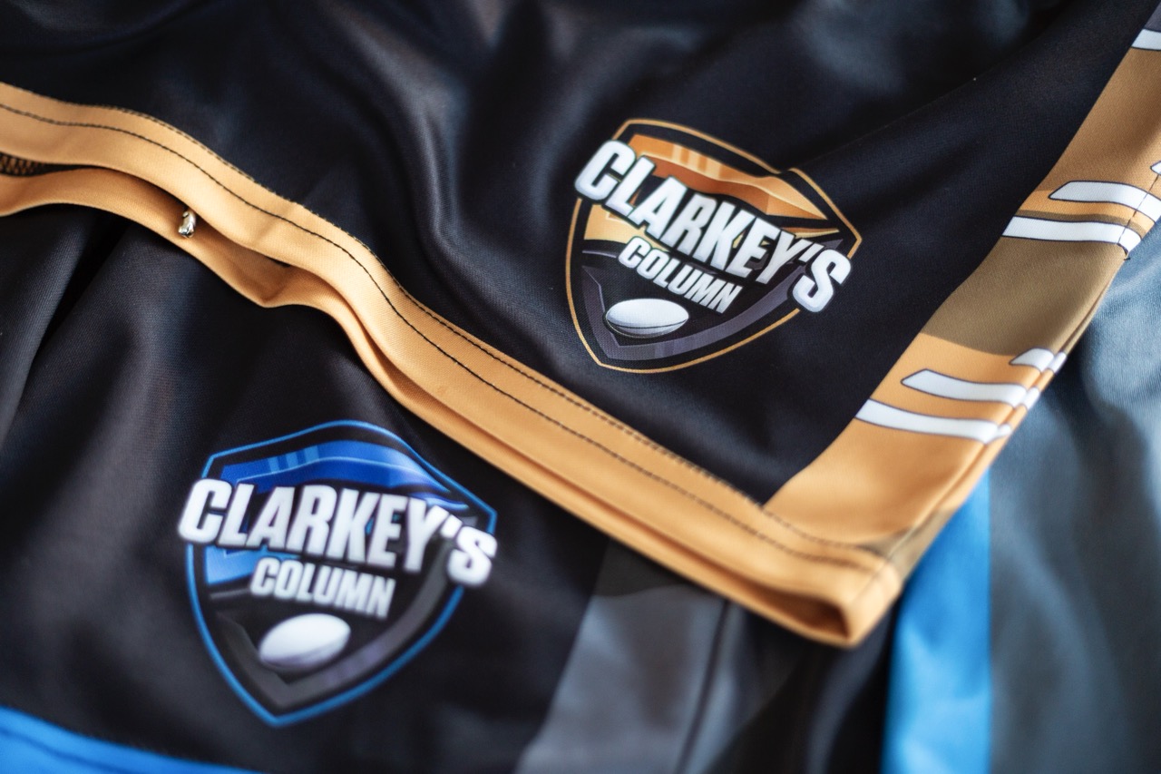 A close up of two pairs of shorts (one blue, one gold) with the Clarkey's Rugby League Column logo on them.