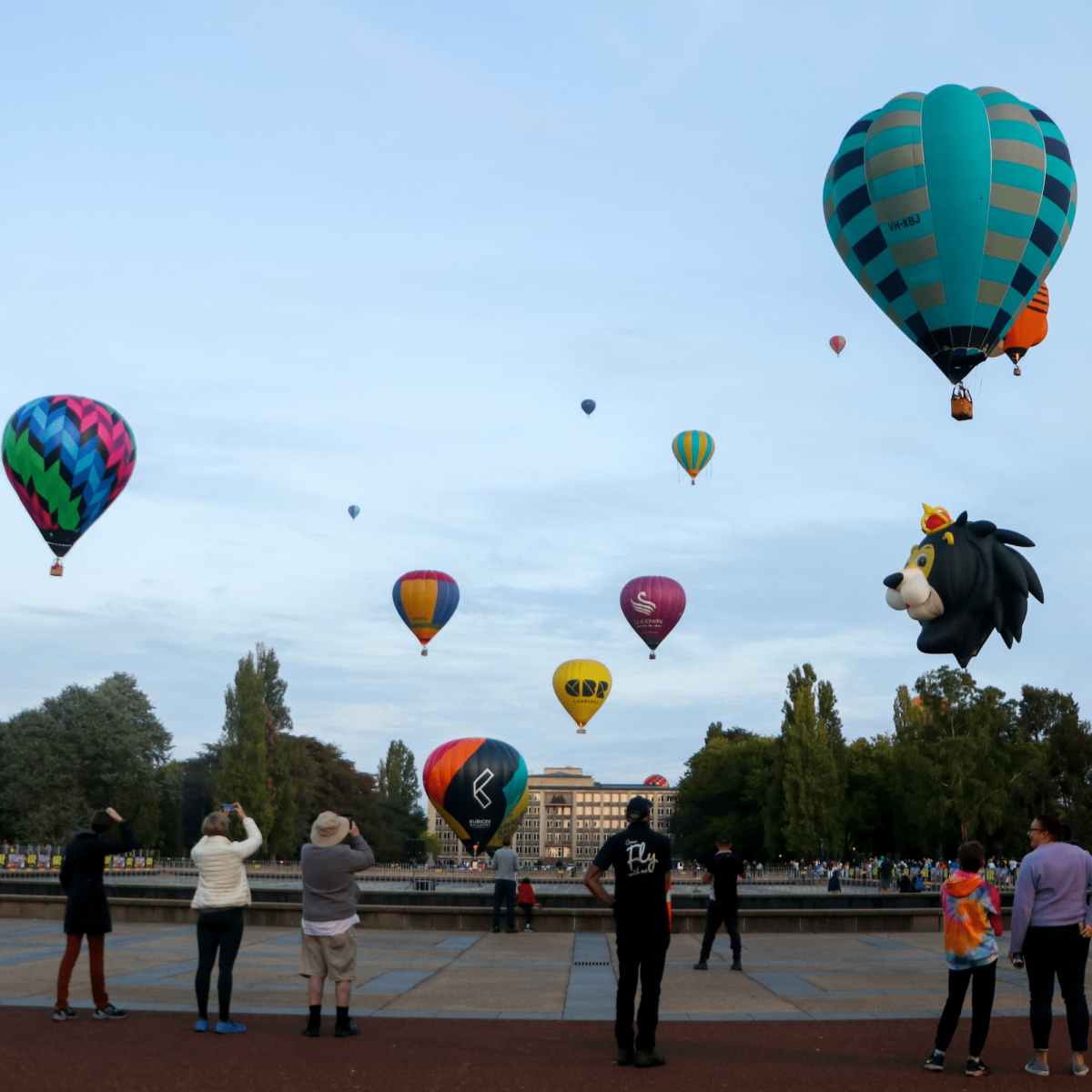 A crowd watches as colourful hot air balloons lift off into the early morning sky.
