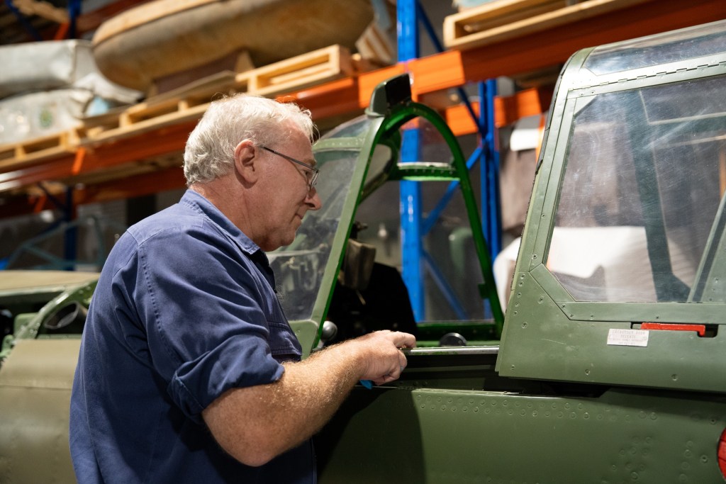 George Bailey looking into the cockpit of Polly, a P-40 Kittyhawk flown by Buster Brown in the Second World War.