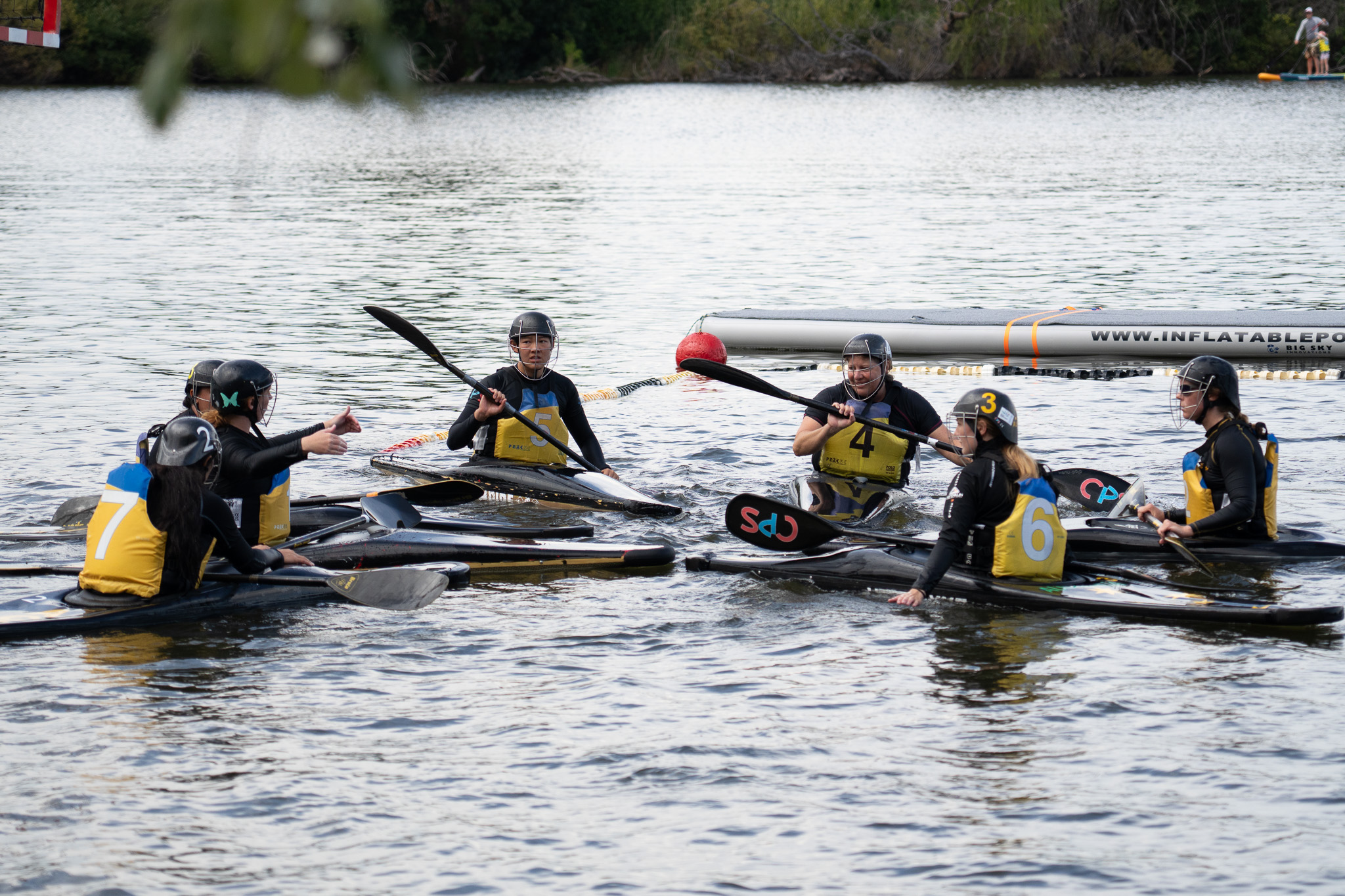 A group of women each sitting in kayaks and wearing protective gear are discussing