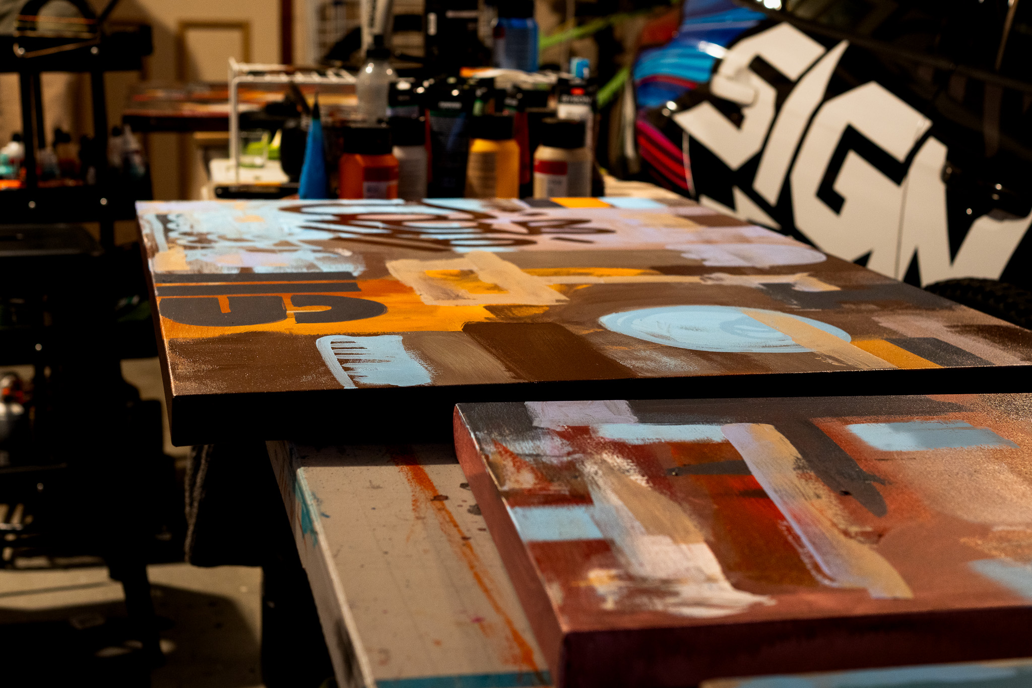 A close up of two different artworks in early stages of creation with art supplies in the background.