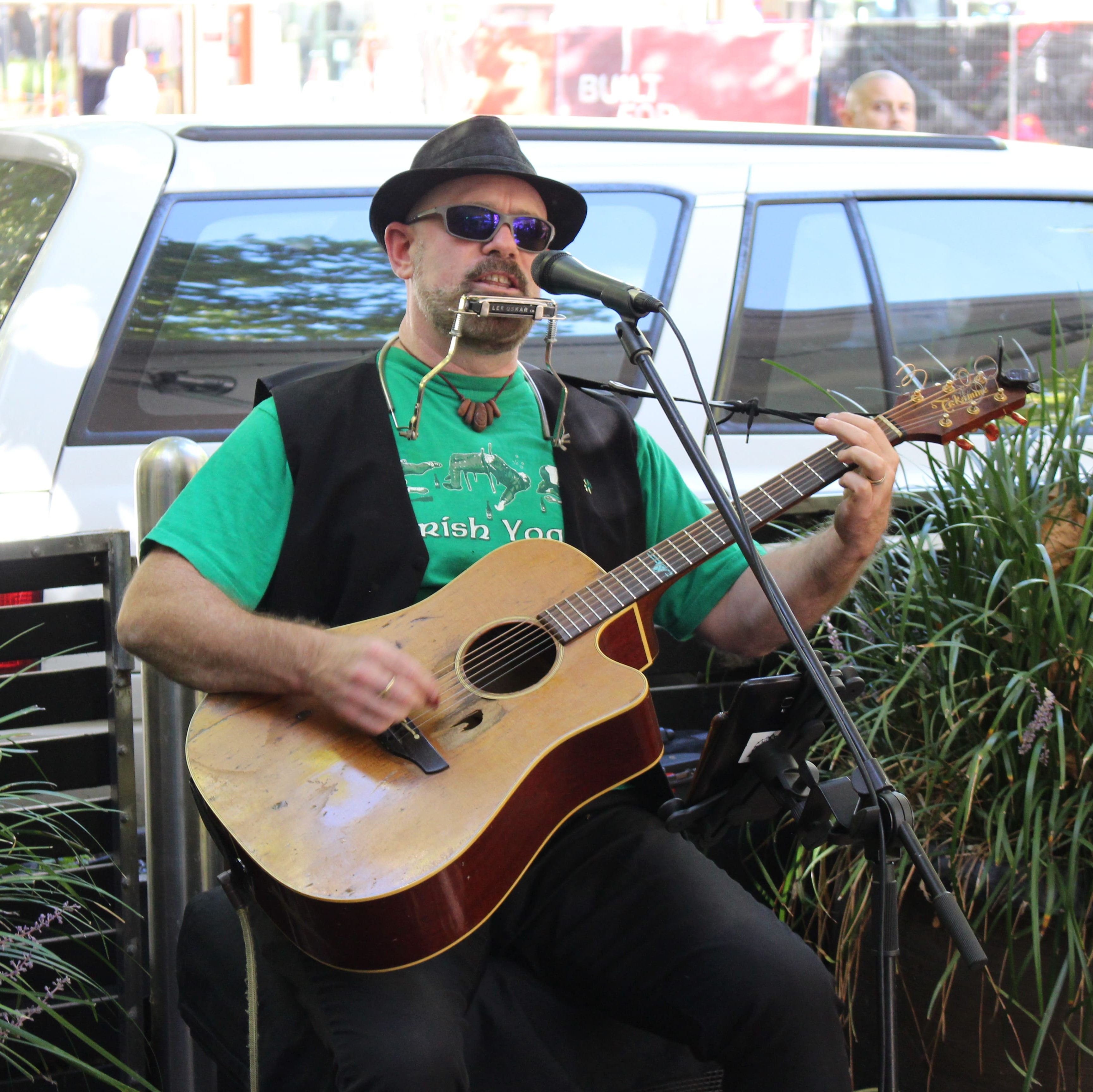 A musician performs a song on guitar and harmonica, singing into a microphone.