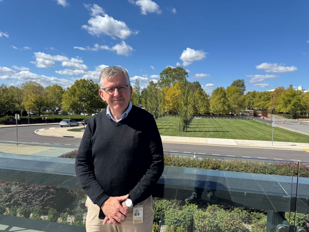 Guy Hansen facing the camera in front of a backdrop of the front lawns of the National Library