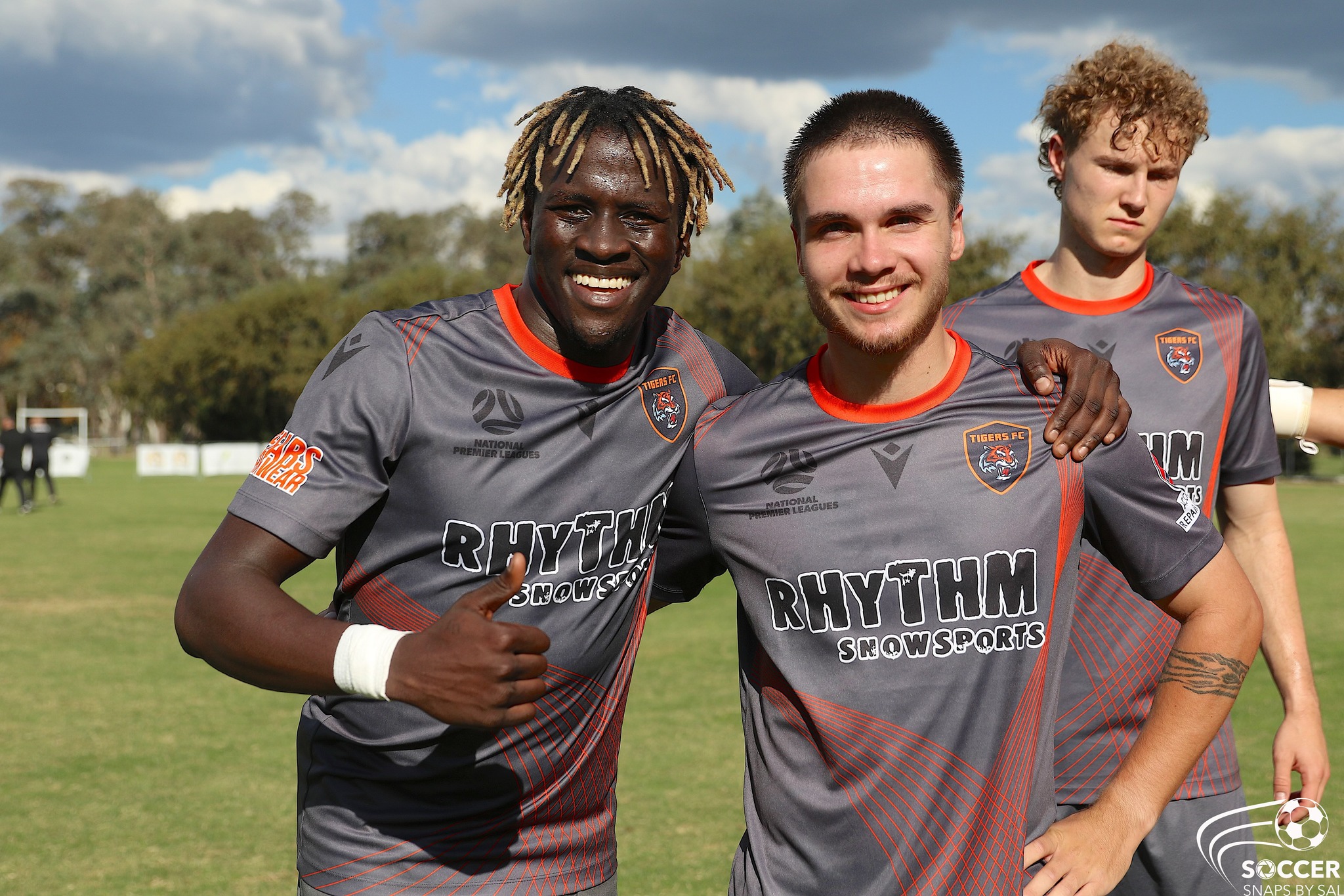 William Akio poses with thumbs up with his arm around his teammate, on a football field