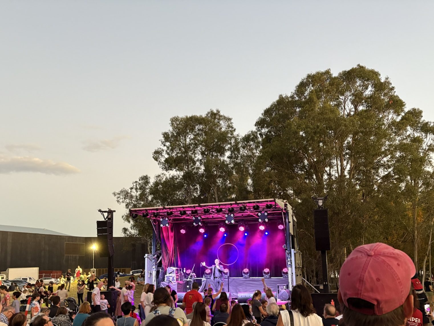 Photograph of a stage with bright purple lights at sunset, with a crowd