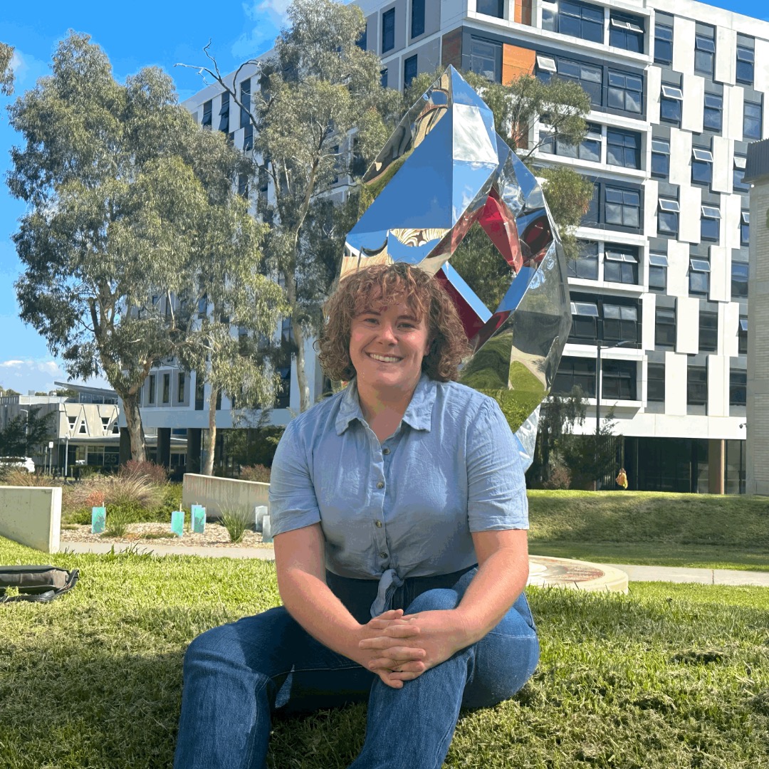 Isabel Mudford sitting on grass in front of silver sculpture.