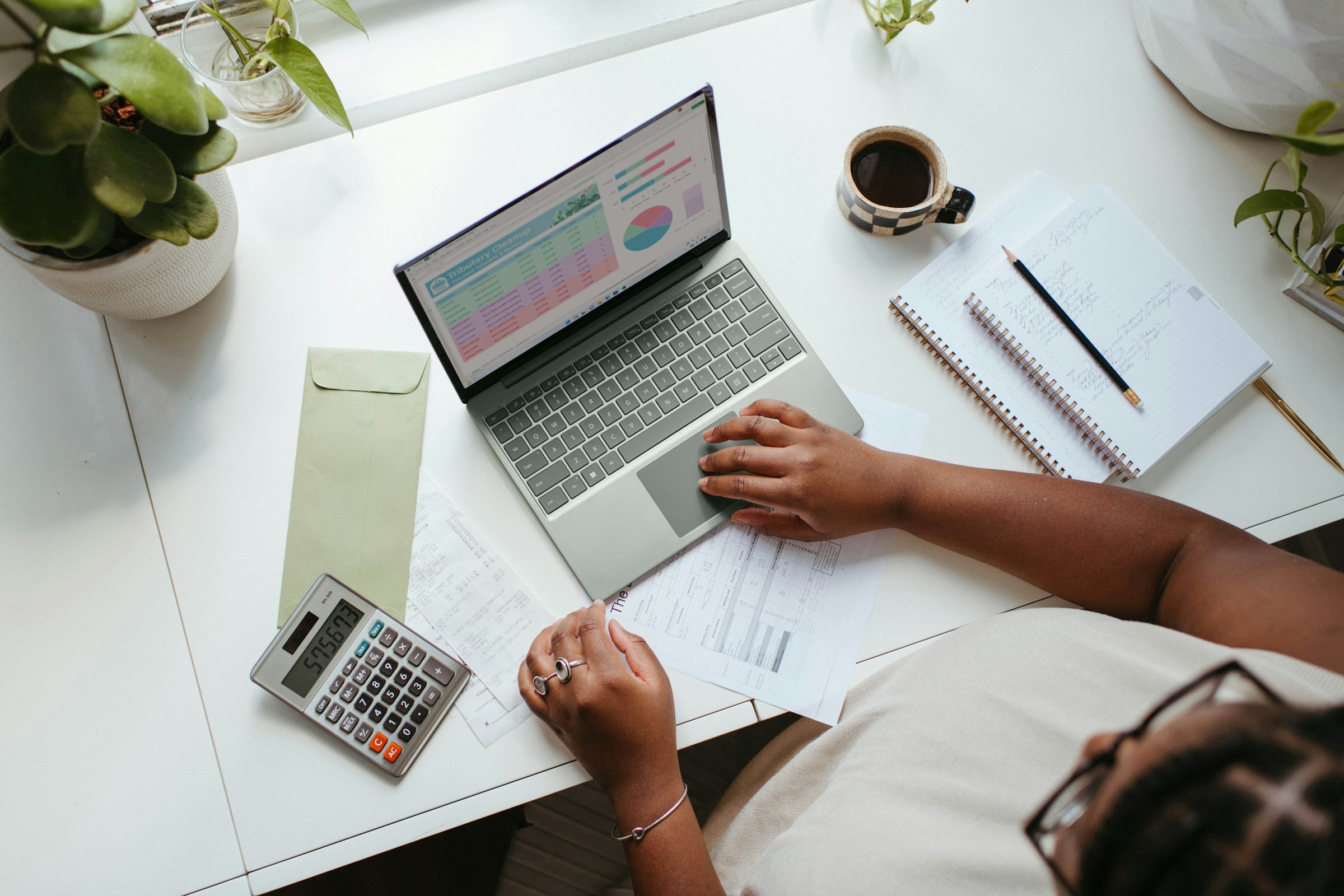 A woman uses a calculator and a laptop to plan a budget