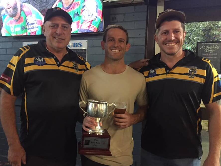 Three men smiling with jerseys, middle man holding a trophy and beer