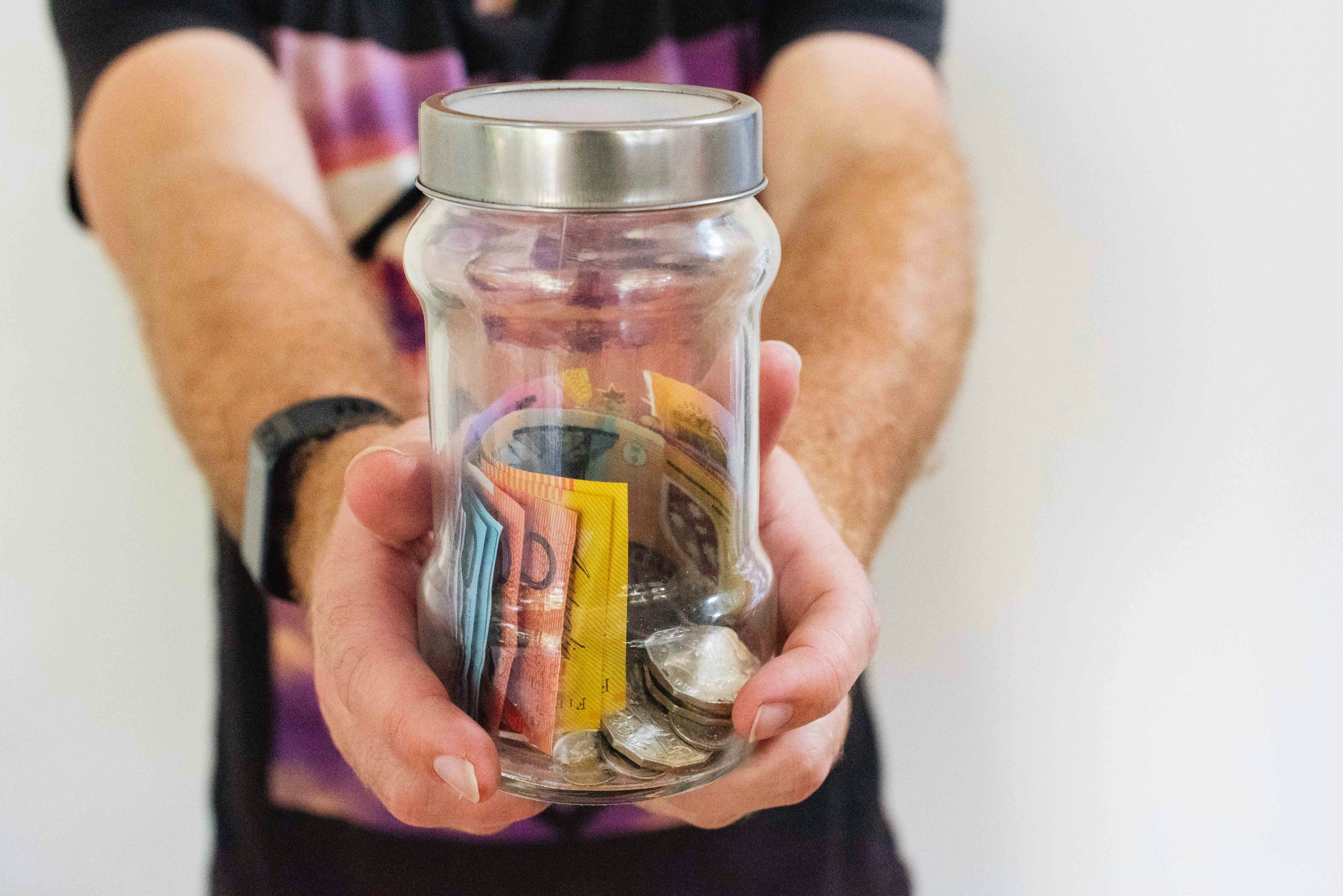 Person holding a jar containing Australian money notes and coins