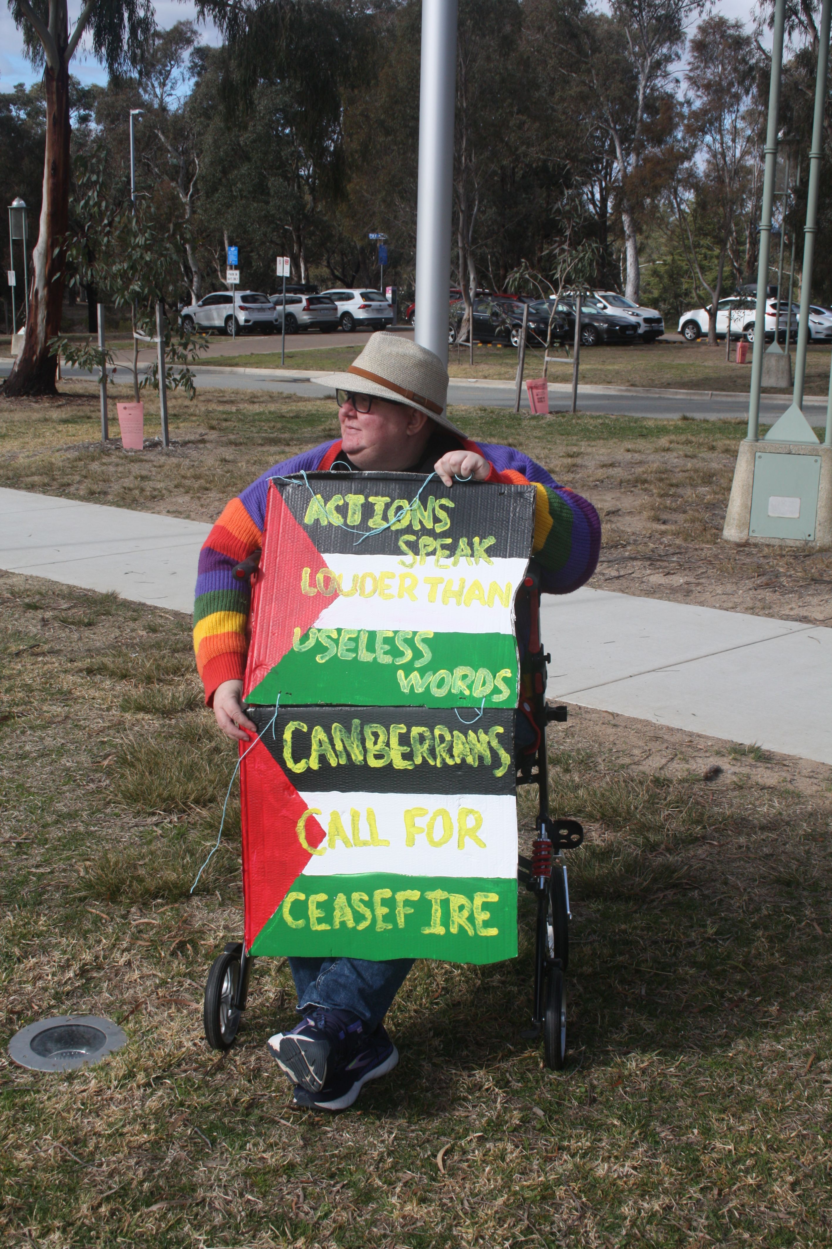 A protestor sitting on a mobility device, holding a handmade sign supporting Palestine.